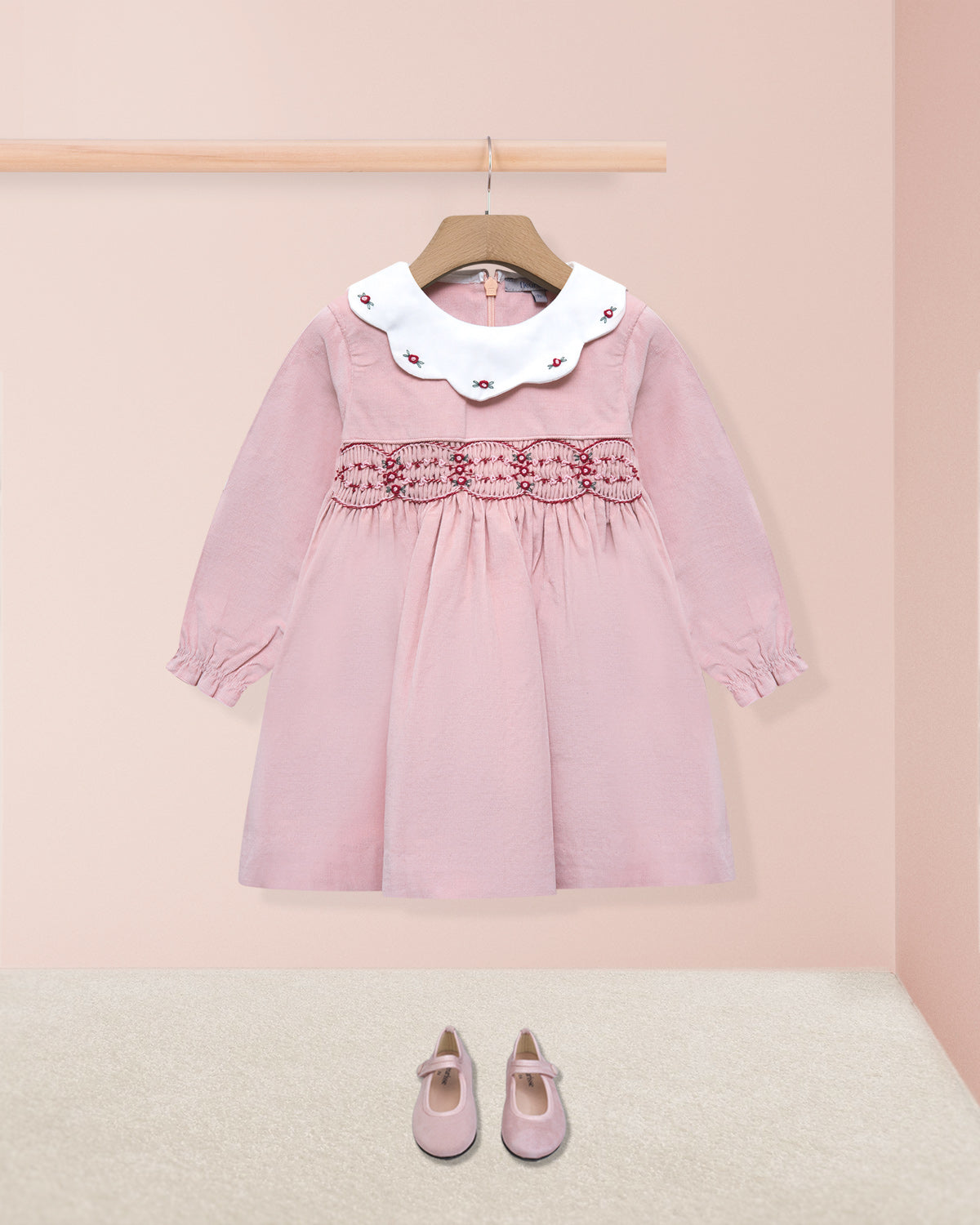 Pink dress with white collar on a hanger against a pink background