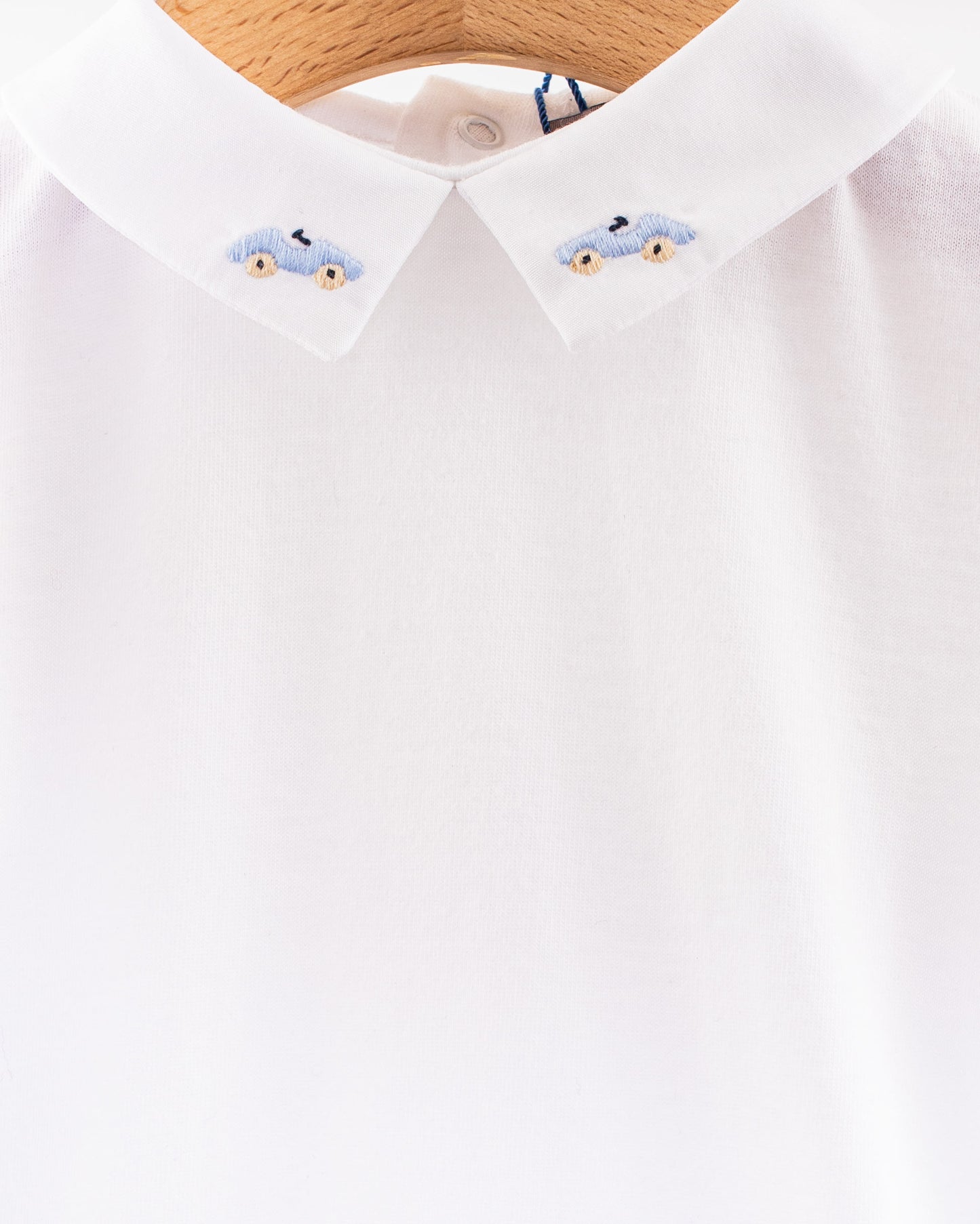 Close-up view of the white cotton onesie's collar, featuring detailed embroidery of two light blue cars with beige wheels on each collar point.