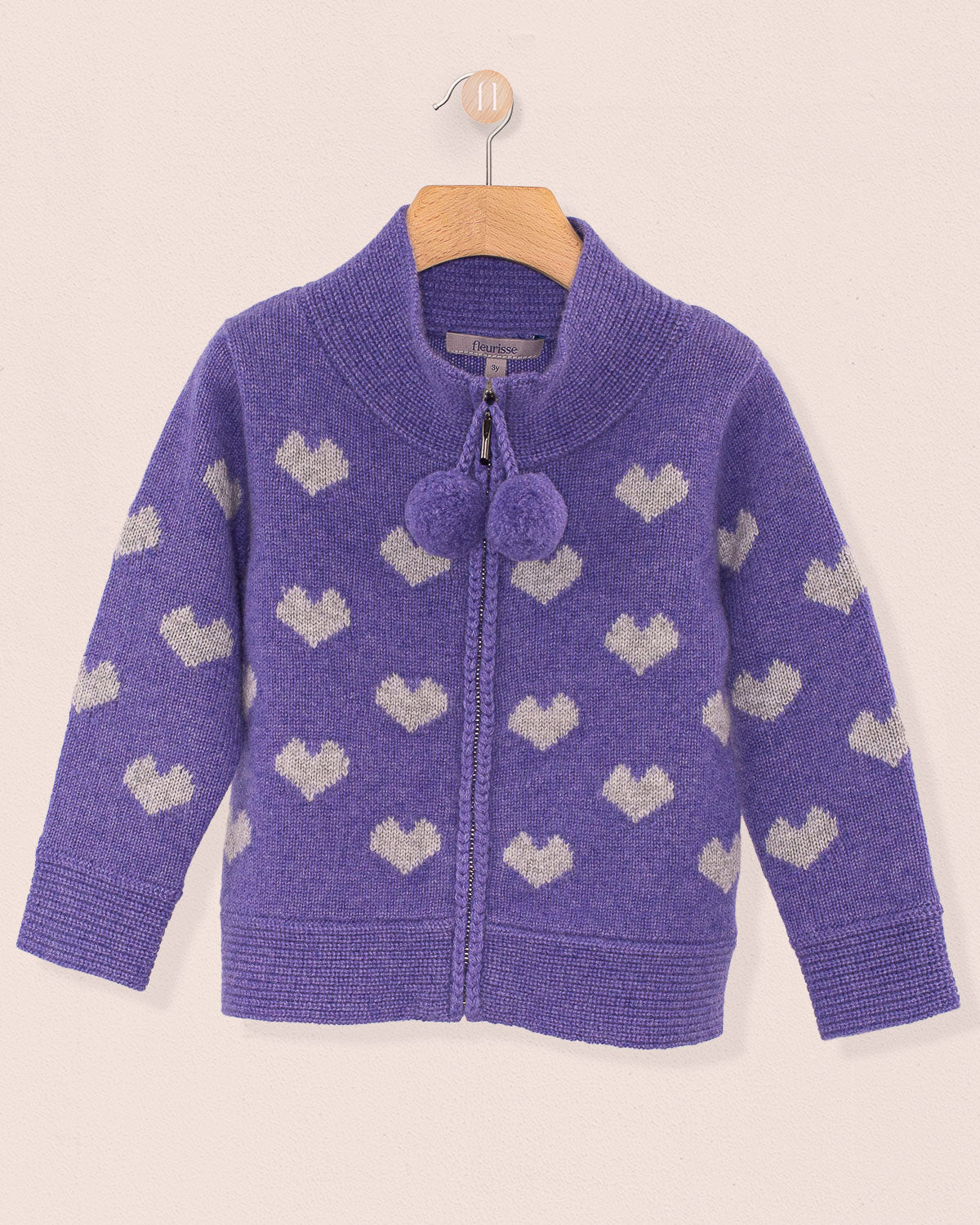 Aspen Cashmere Lavender Hearts Zipper Sweater with ribbed hem and cuffs, shawl collar, and purple pom-pom zipper pulls, hanging on a wooden hanger.