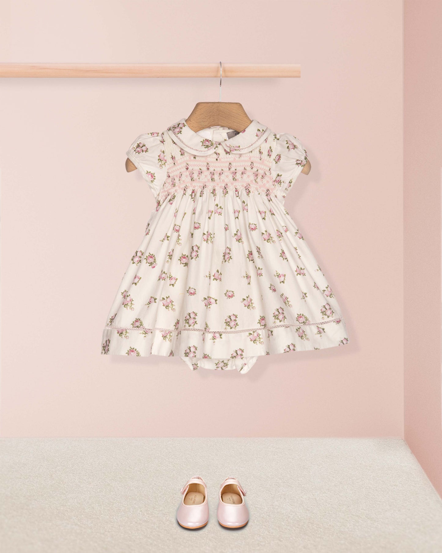 Floral dress on a hanger with pink shoes on the floor against a pink wall
