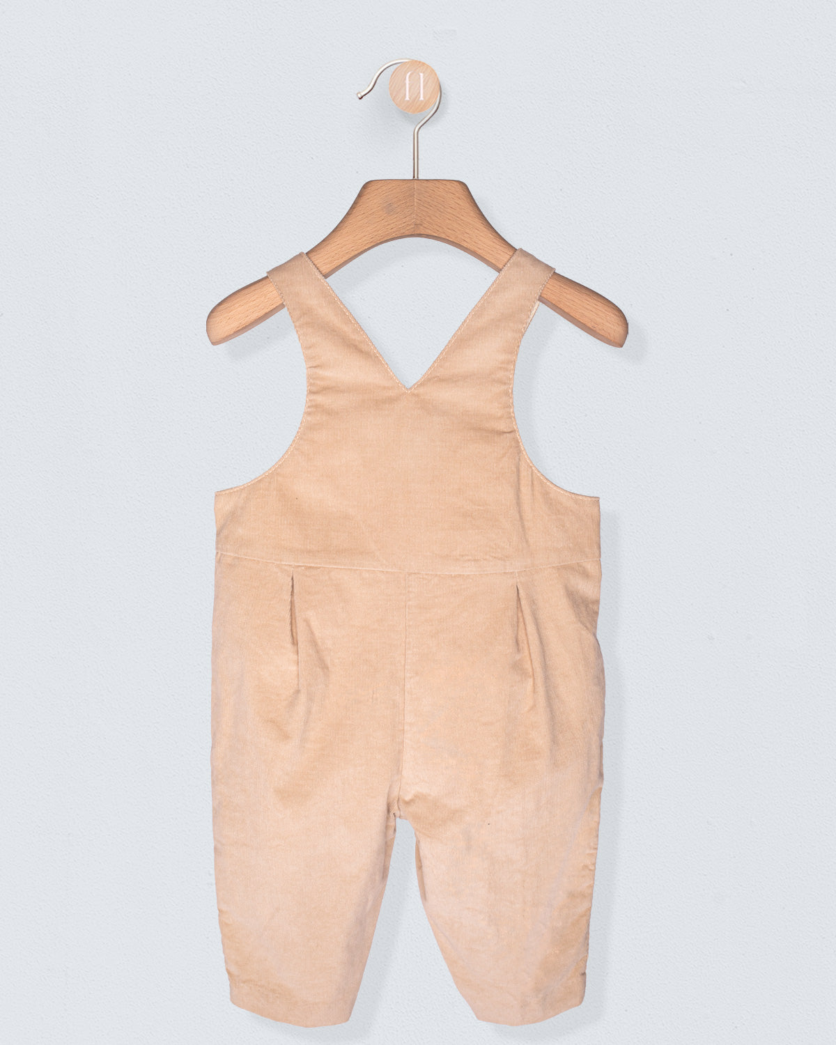 Beige overalls hanging on a wooden hanger against a light gray background