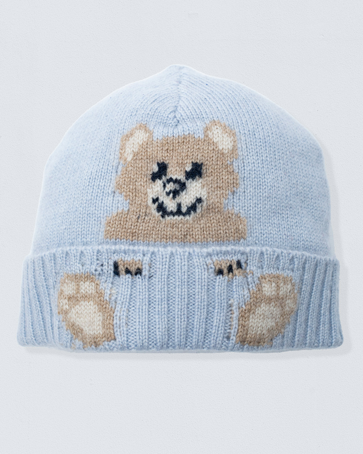 Light blue knit baby hat with teddy bear design on a light gray background