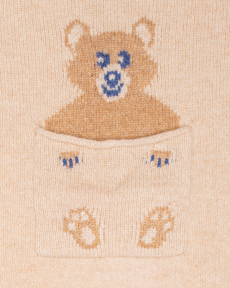 Close up of embroidered design of a bear peeking out from a pocket on a beige cashmere blanket
