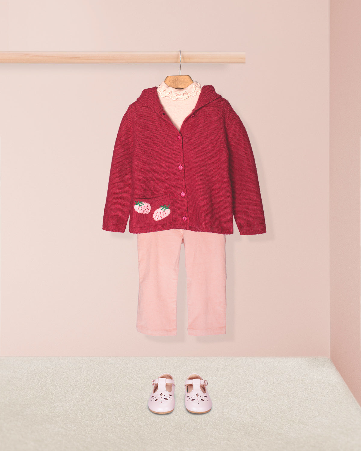 Children's outfit with fuchia jacket and pink pants on a hanger against a light pink wall.