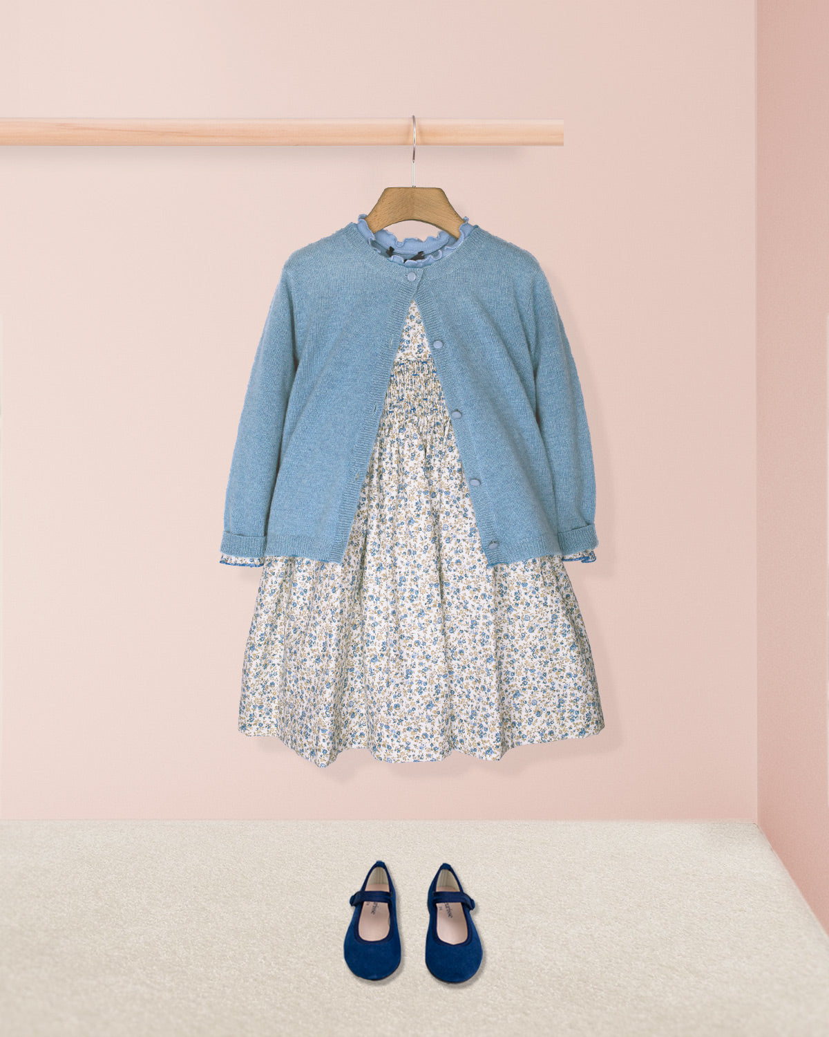 Blue cardigan over a floral dress with matching shoes on a pink background