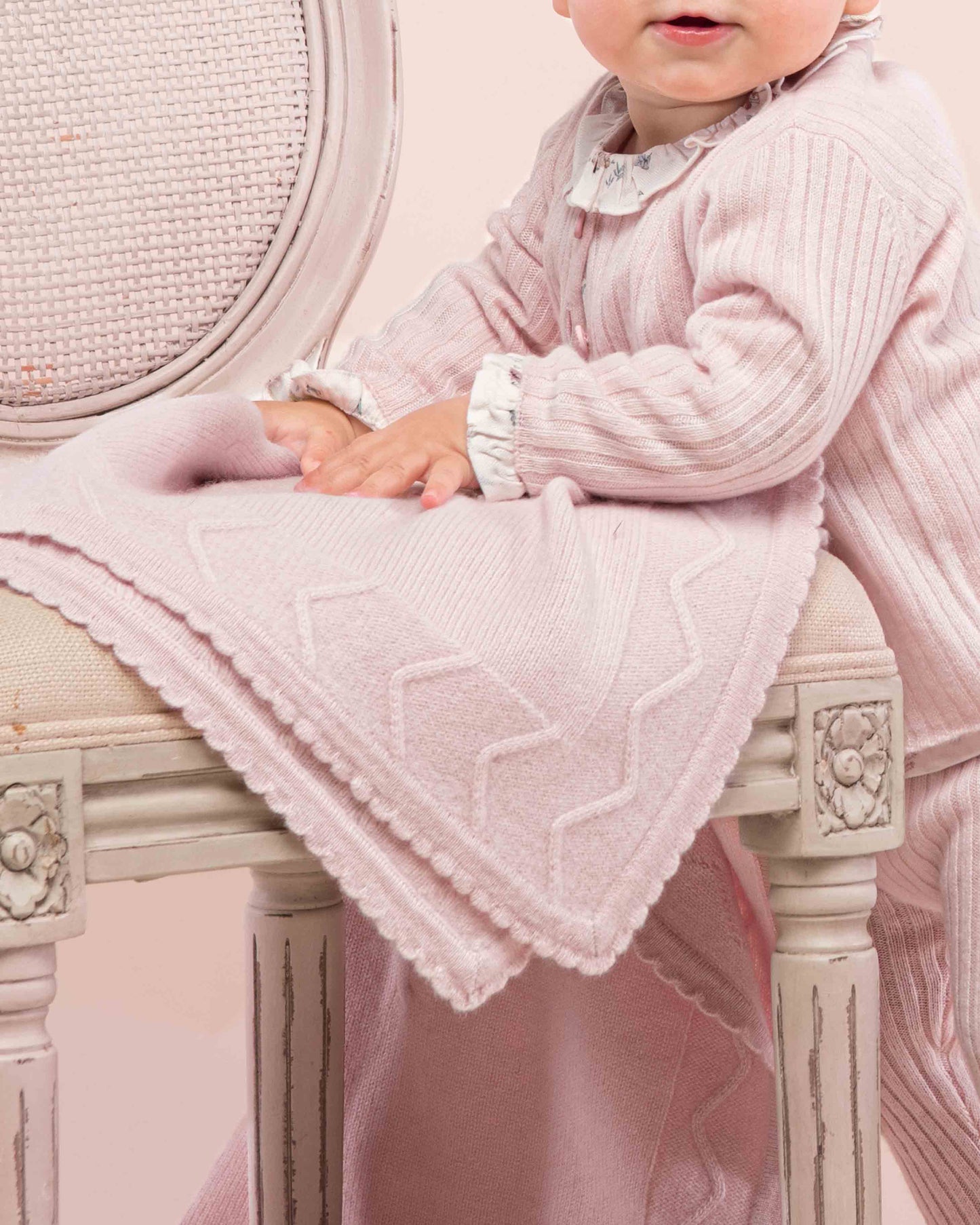 Baby turned to the side, touching the Cherie Cashmere Pink Blanket, showing the trim detail on the blanket