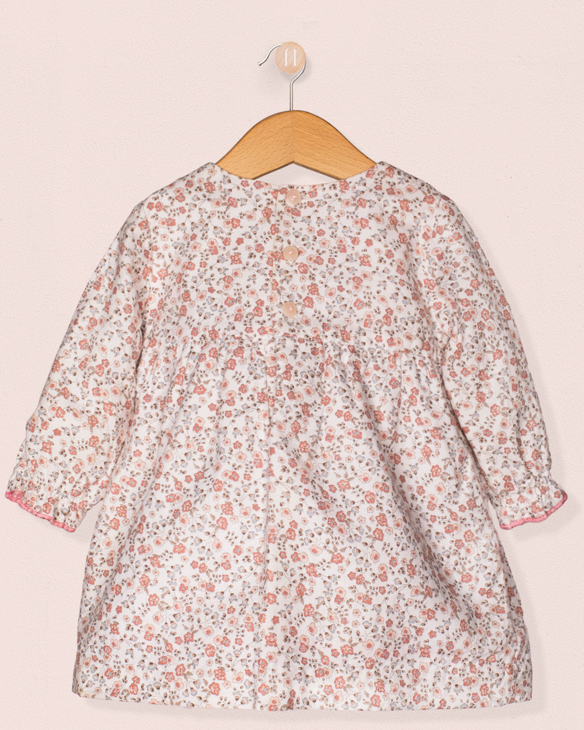 Floral dress on a wooden hanger against a light pink background