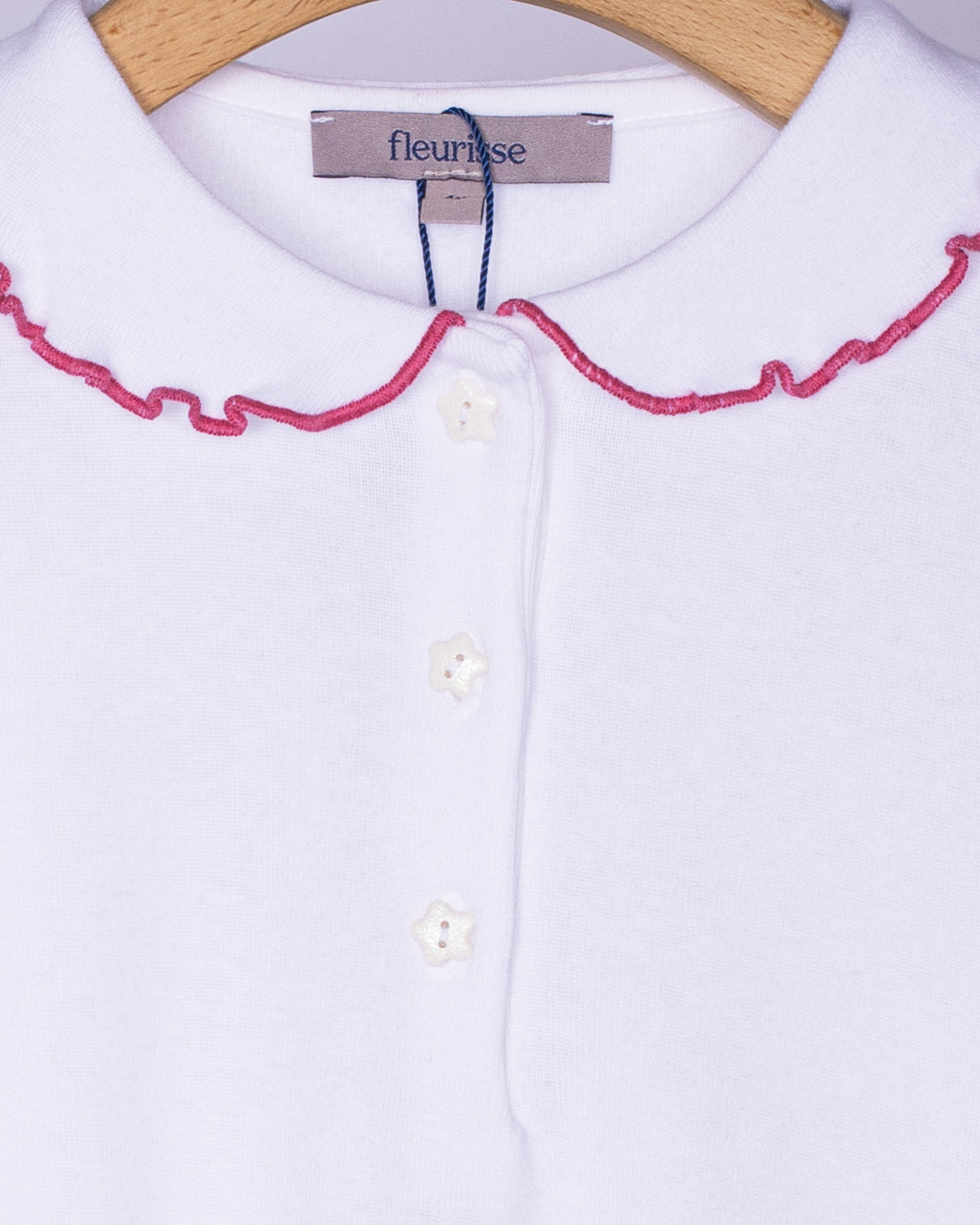 Close-up view of the soft brushed cotton fabric on the white long sleeve shirt, showing the delicate ruffle collar with rose-pink trim and three small white star-shaped buttons on the front placket.