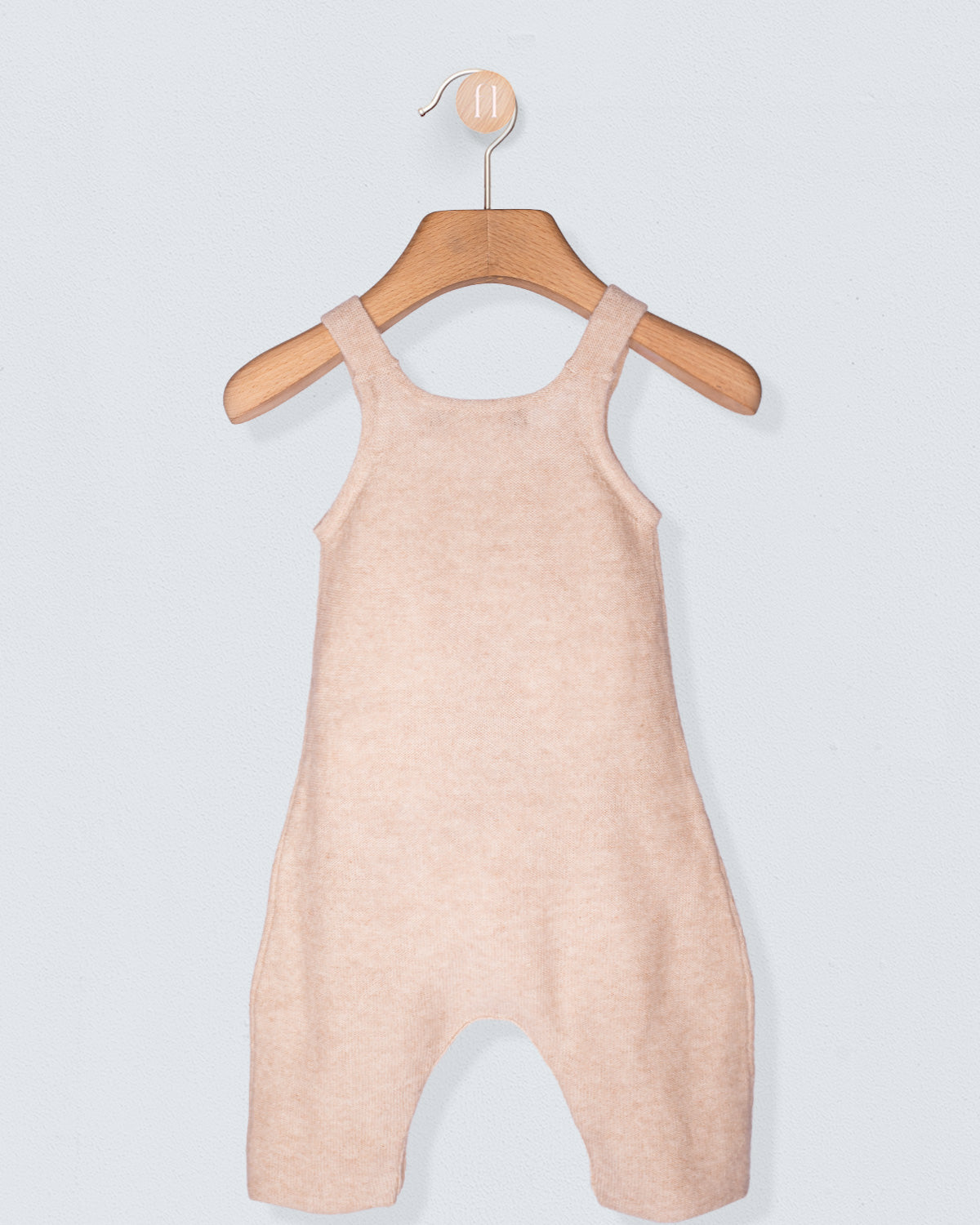 Pink baby romper on a wooden hanger against a light gray background