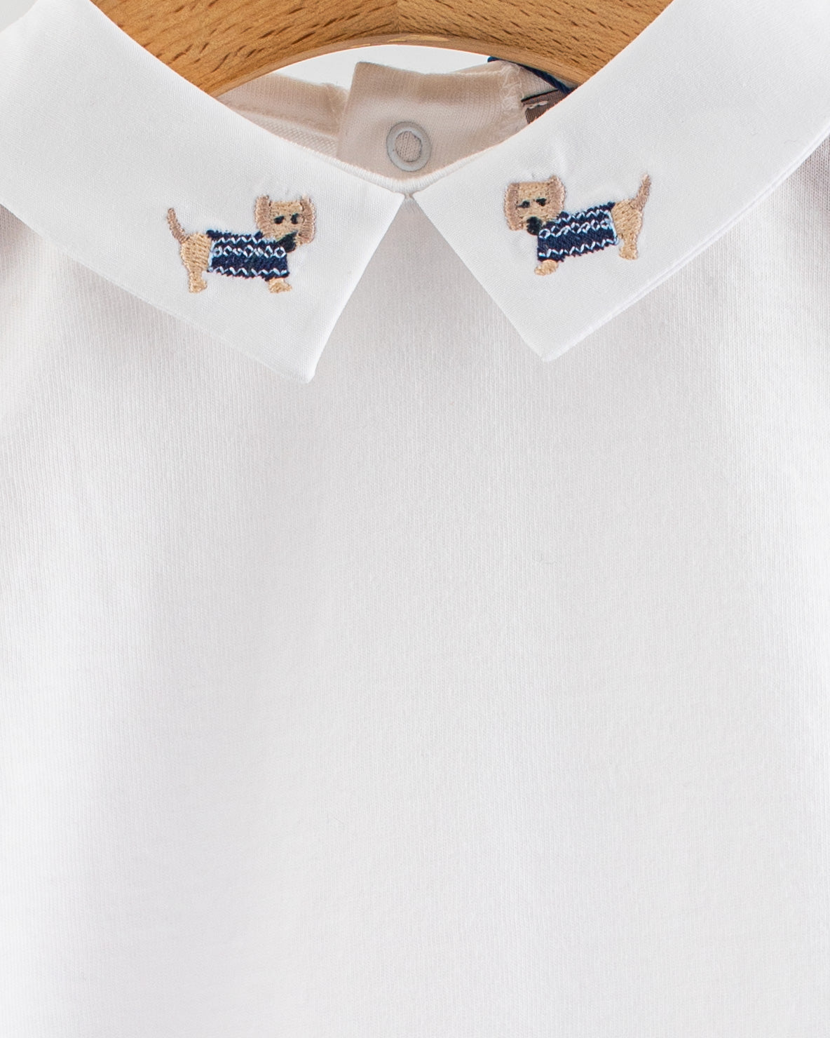 Close-up of the Andreas Onesie collar showing two embroidered beige dachshund dogs wearing navy denim-style sweaters on either side of the collar.