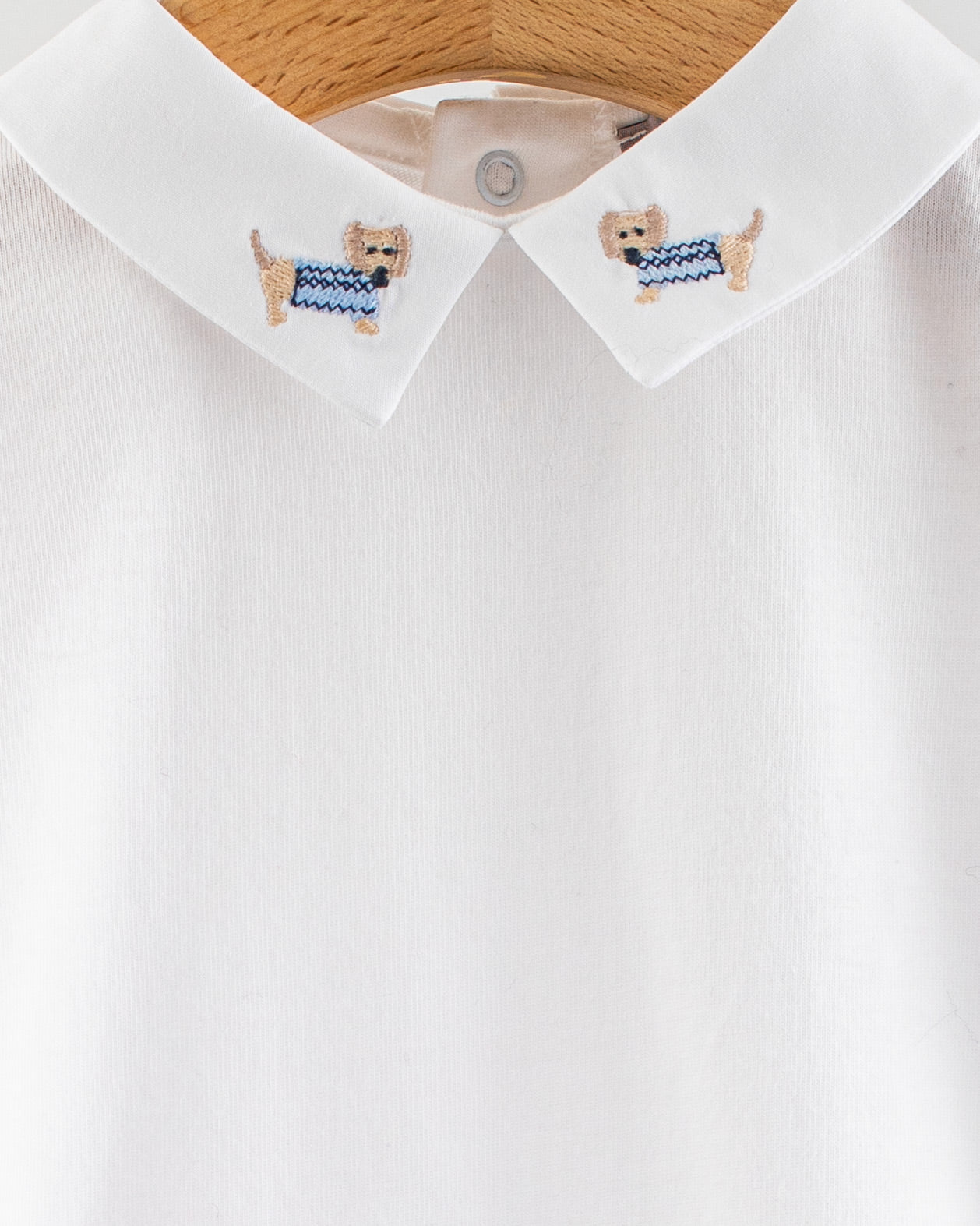 Close-up of the Andreas Onesie collar showing two embroidered beige dachshund dogs wearing light blue sweaters on either side of the collar.