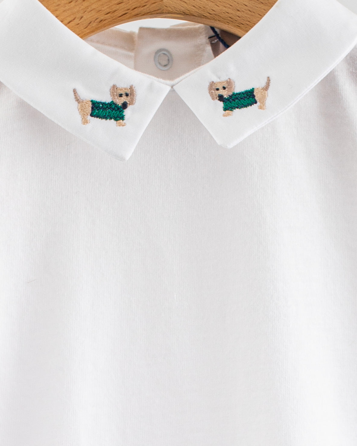 Close-up of the Andreas Onesie collar showing two embroidered beige dachshund dogs wearing sage green on either side of the collar.