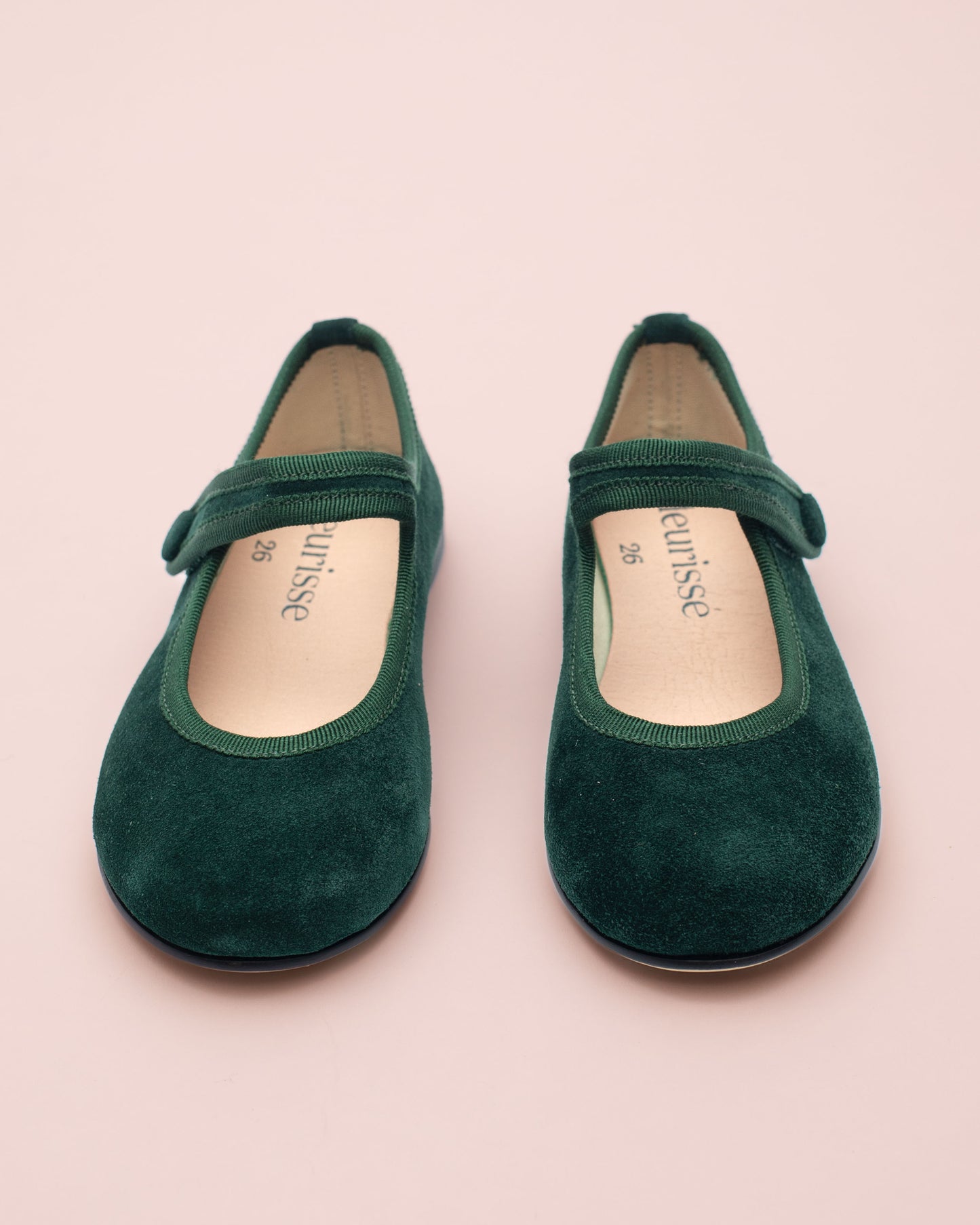 Pair of green shoes with a strap on a pink background