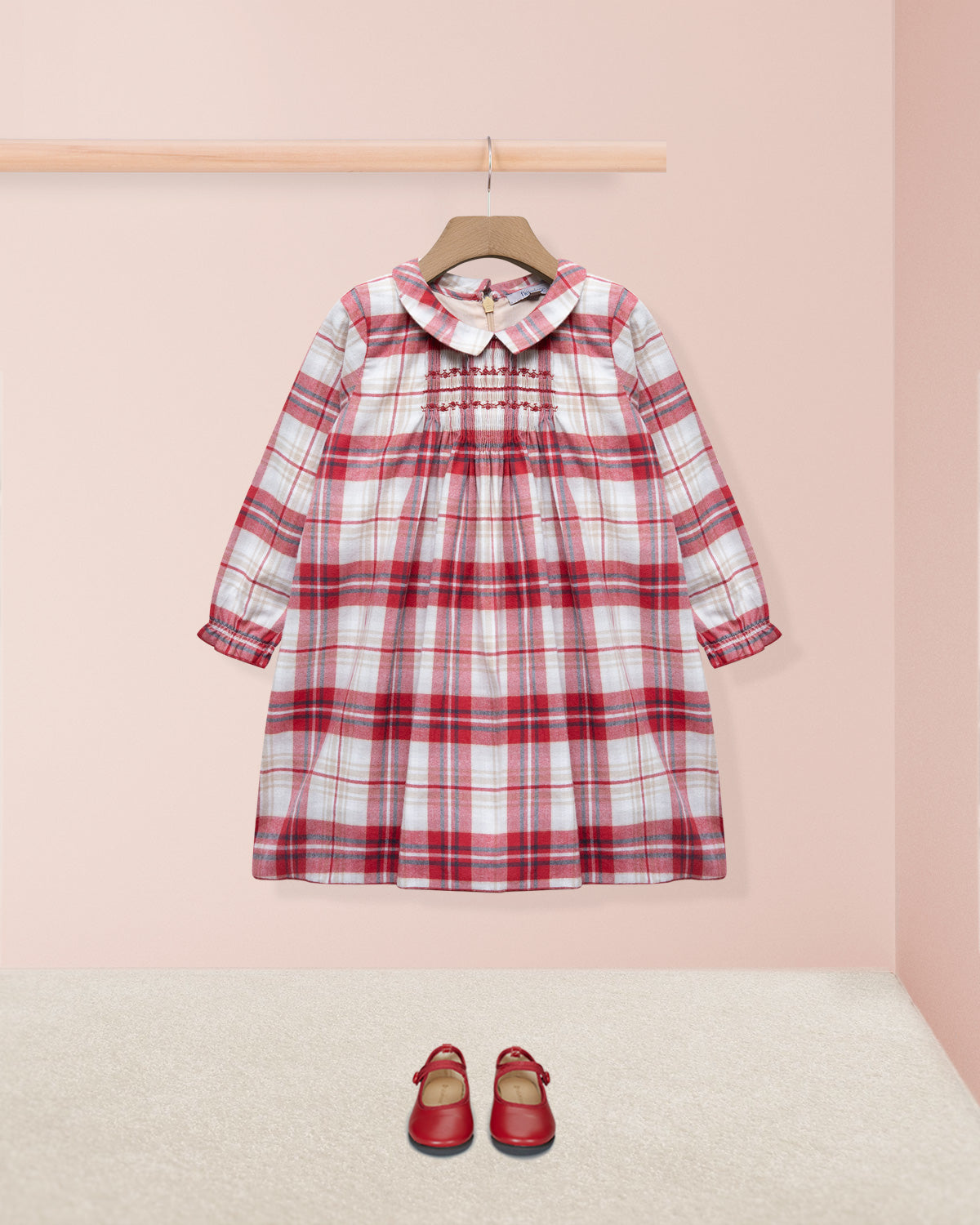 Red and white checkered dress on a hanger with matching shoes on the floor against a pink wall.