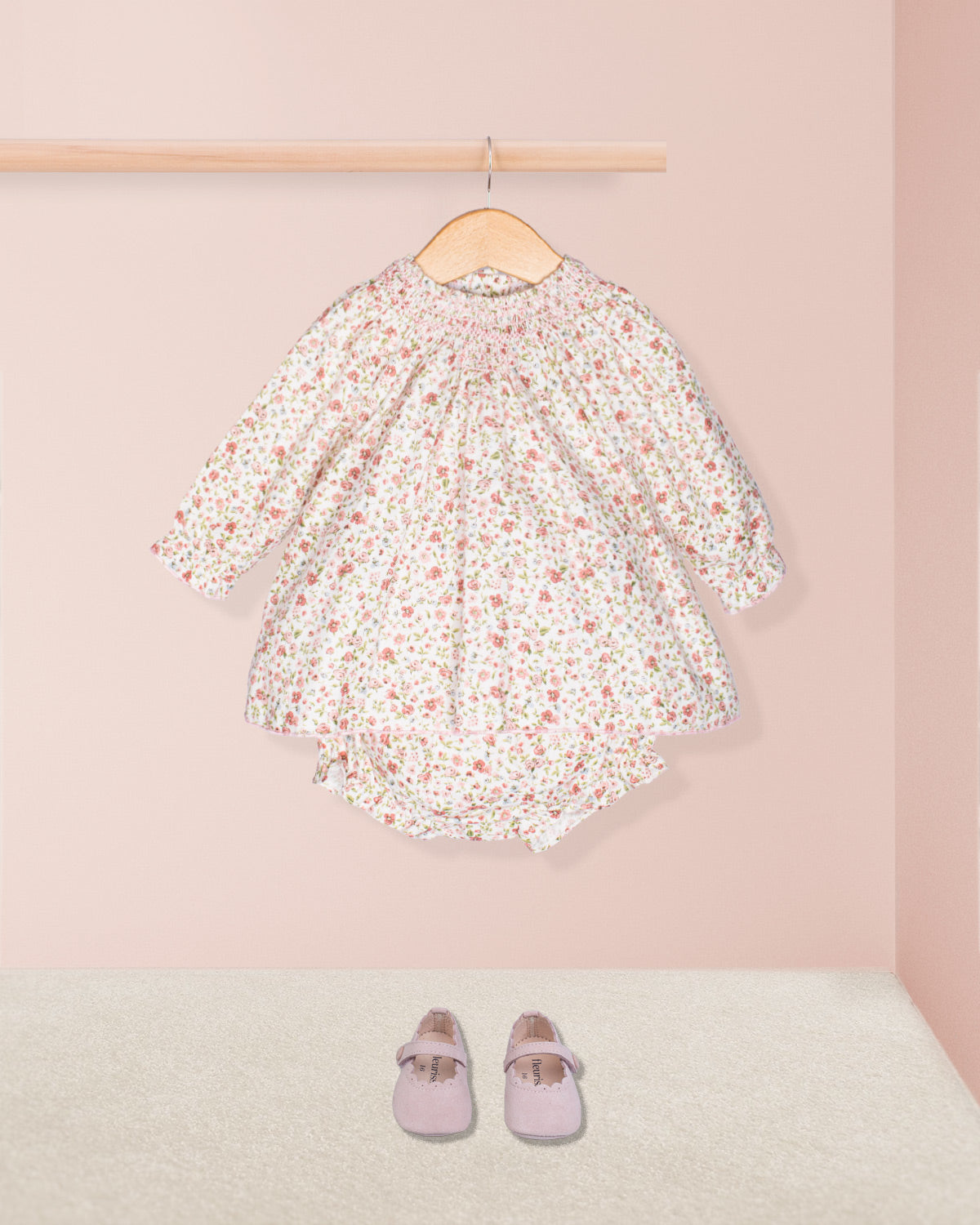Floral dress on a hanger with pink shoes on the floor against a pink wall