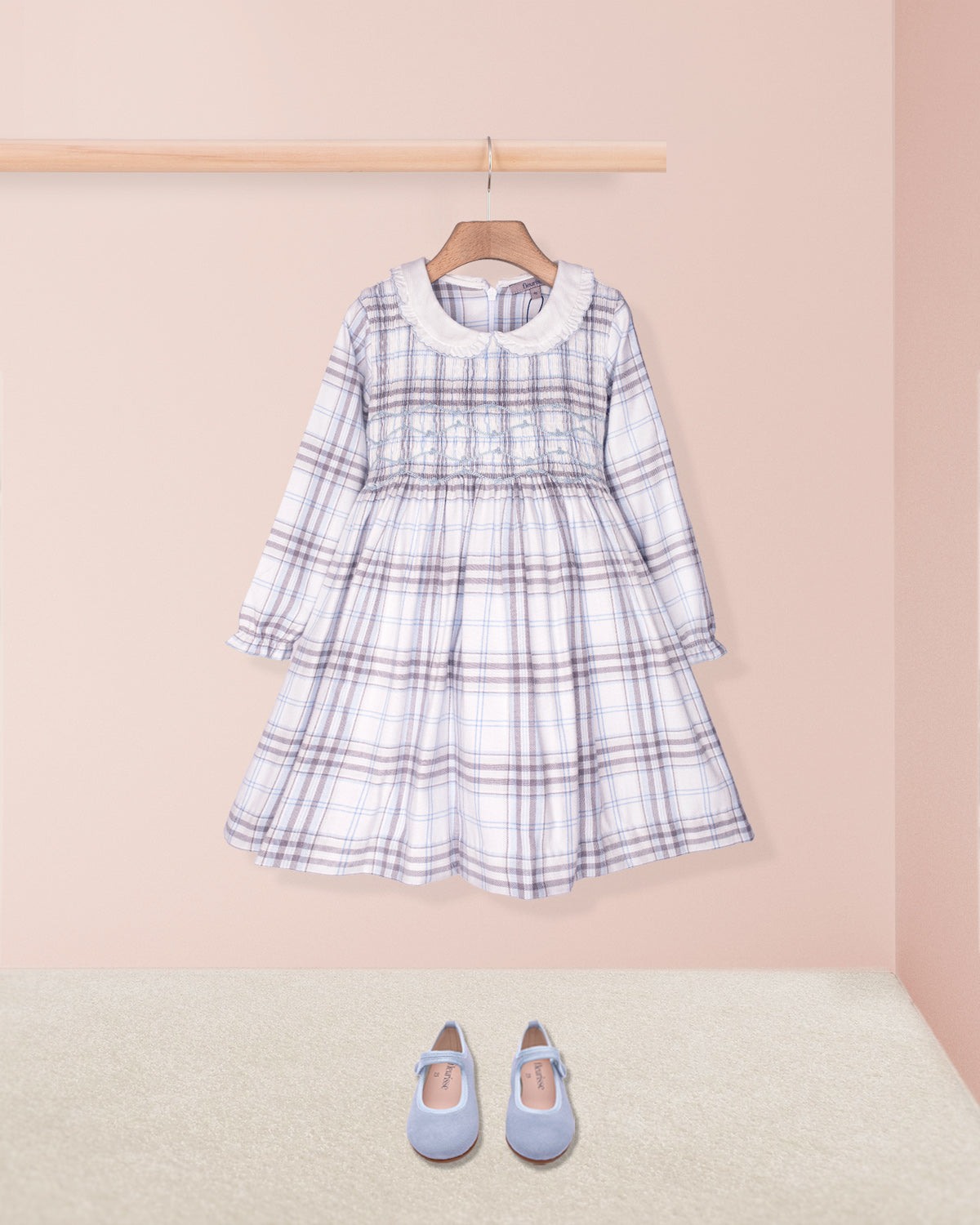 Plaid dress with long sleeves and a collar on a hanger, accompanied by blue shoes on a beige floor.