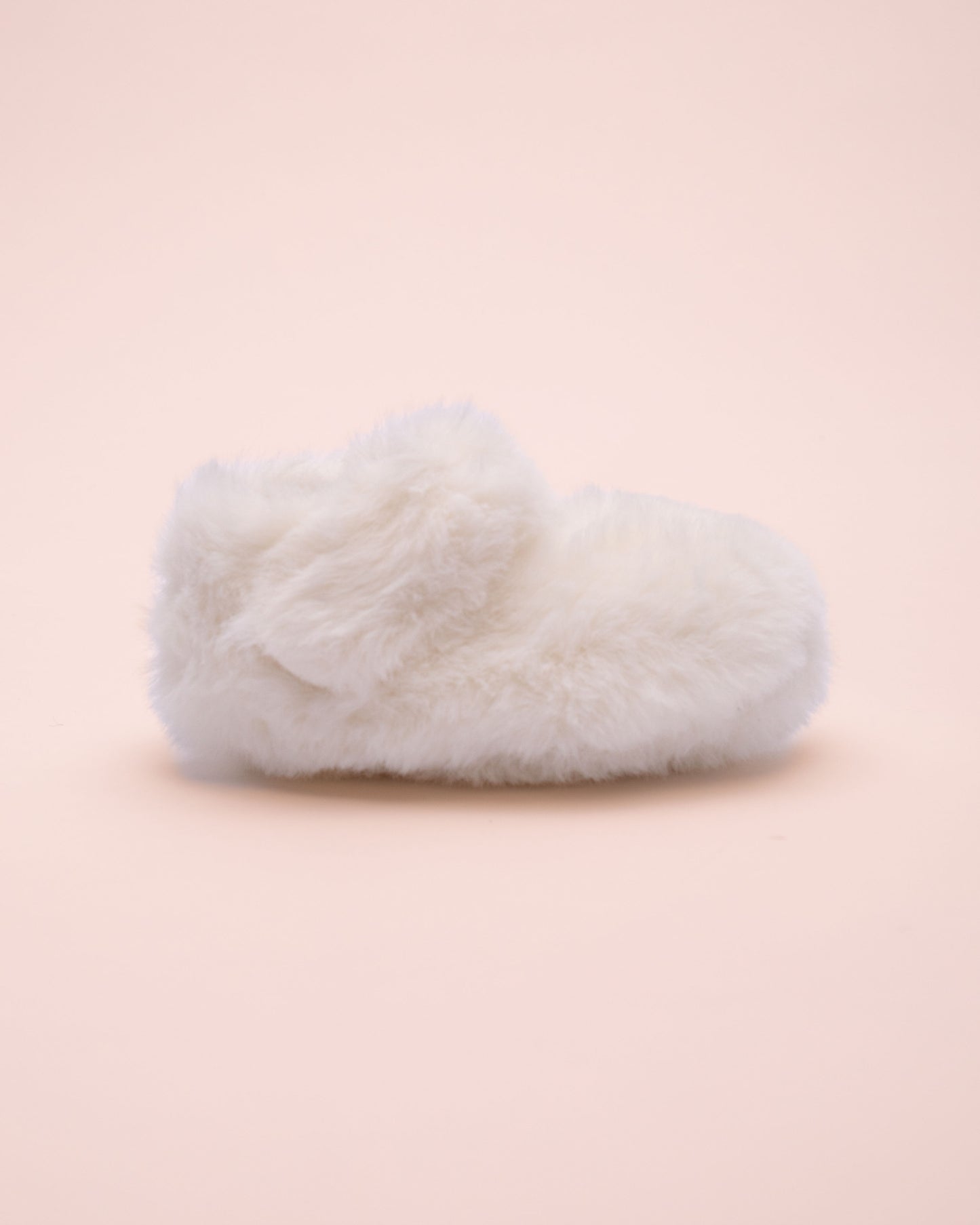 White fluffy crib shoe side view on a light pink background