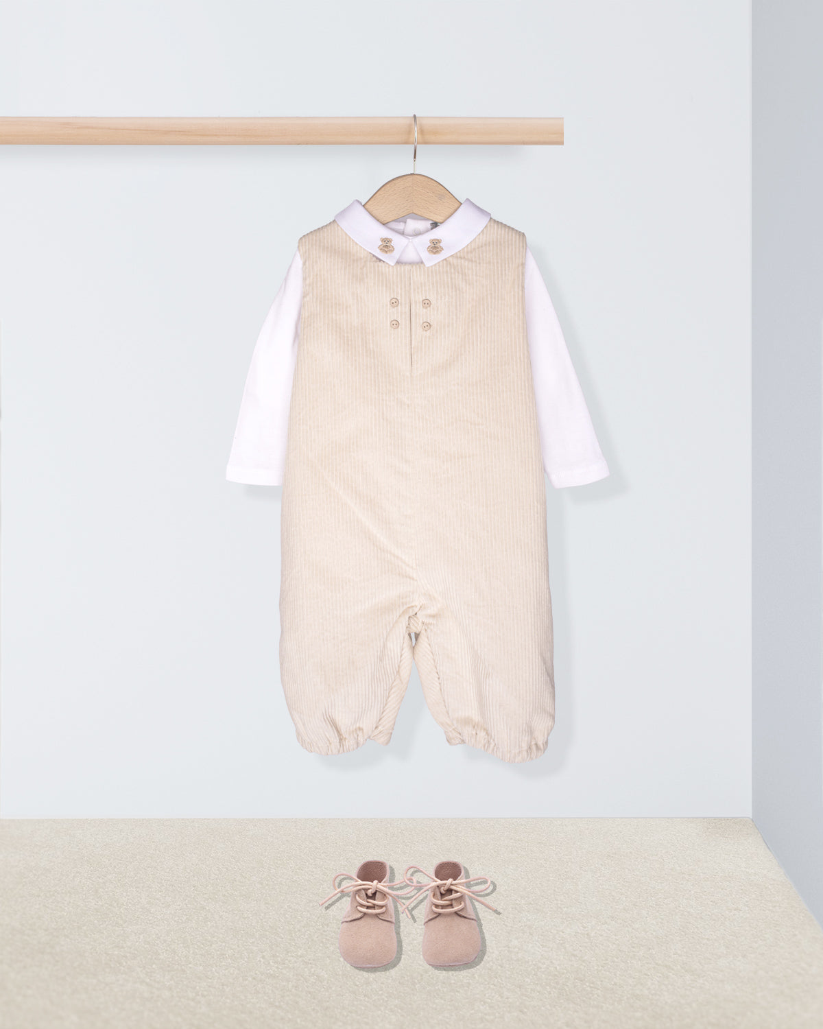 Beige baby romper with white shirt and pink shoes on a light gray background