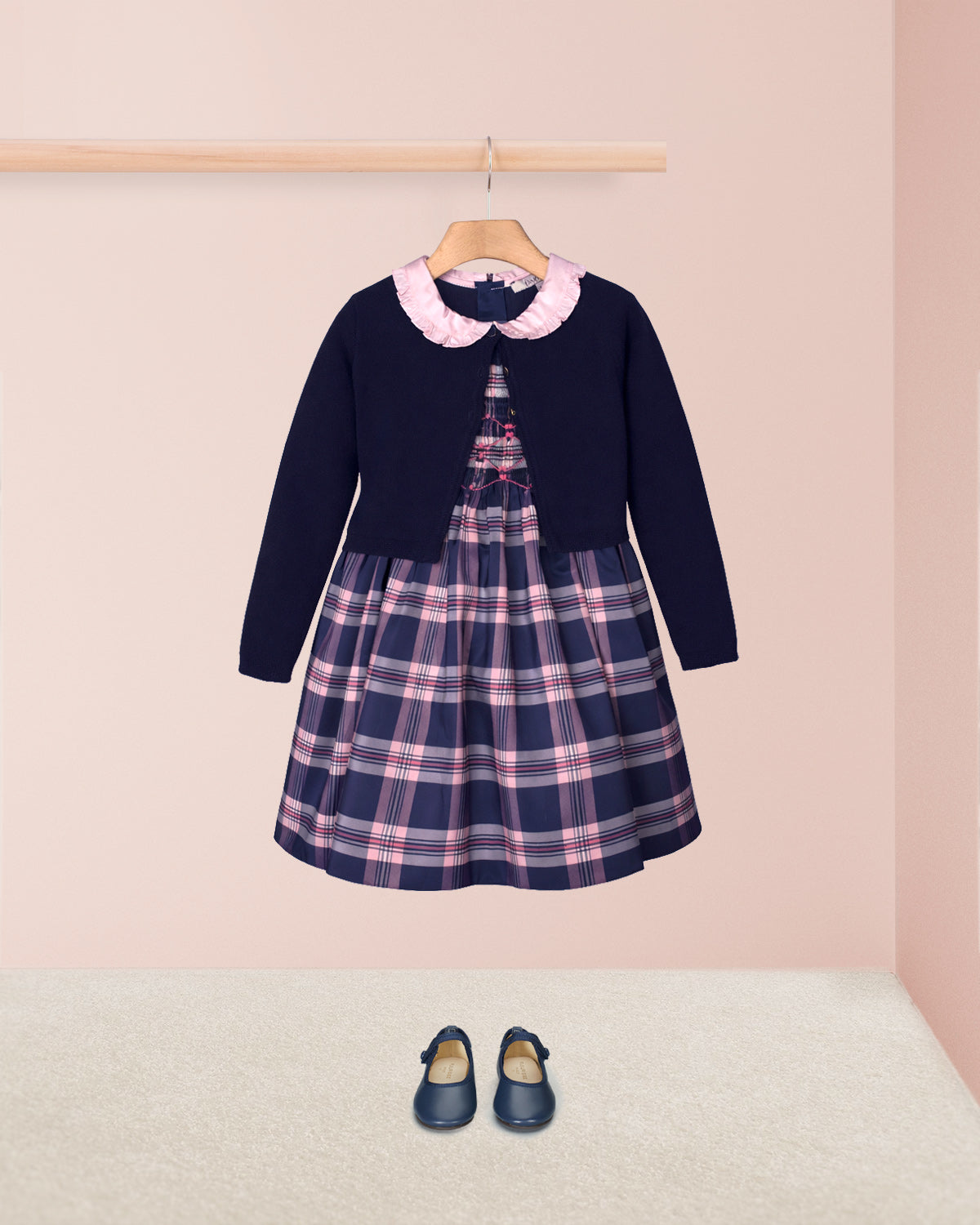Navy dress with plaid pattern and pink collar on a hanger against a light pink background.