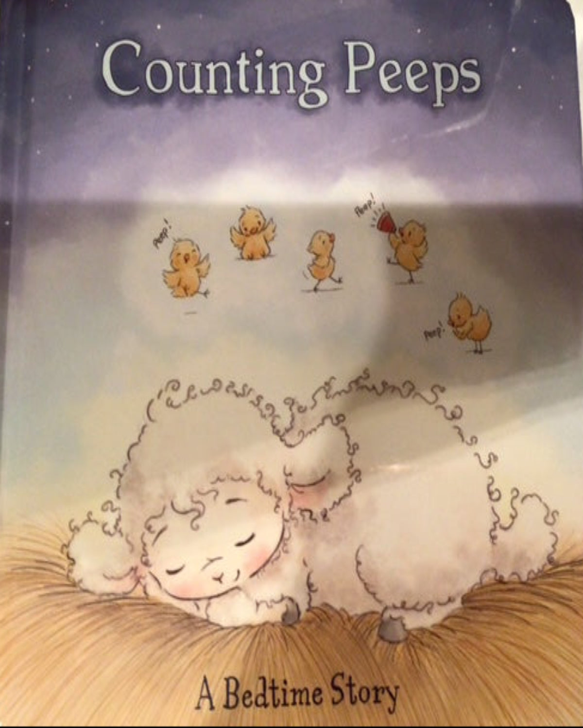 Book titled 'Counting Peeps' with illustrations of a sheep and small animals on a wooden surface.