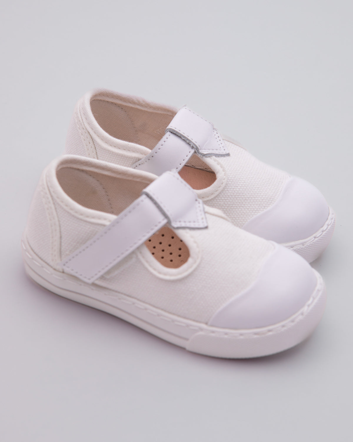 Pair of white blue canvas toddler sneakers with white rubber soles, tonal white leather toe caps, and velcro straps, placed at a slight angle on a gray background.