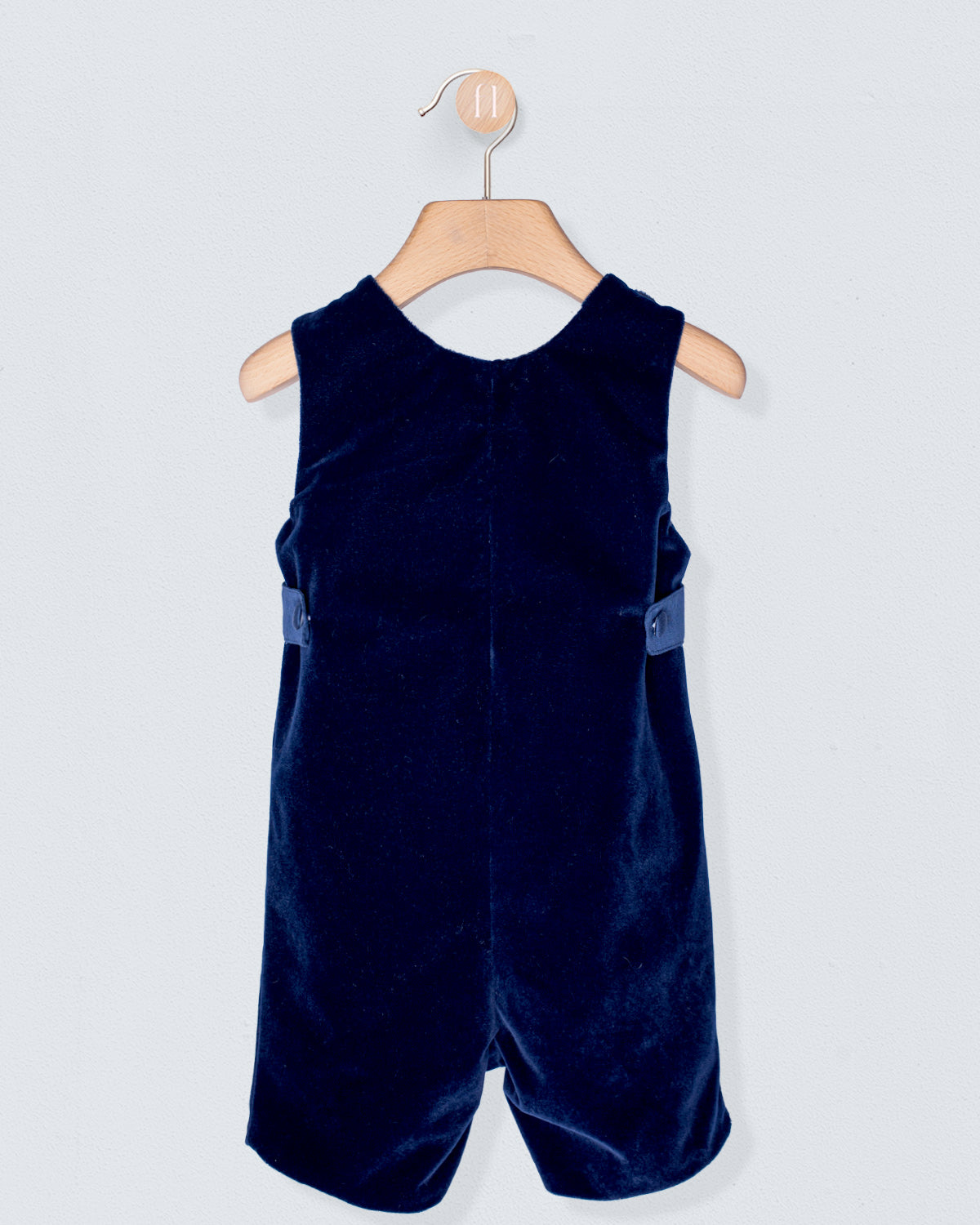 Navy blue velvet romper on a wooden hanger against a light gray background