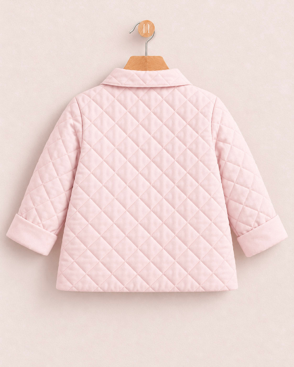 A light pink quilted jacket with long sleeves and a collar, shown from the back on a wooden hanger against a light beige background.
