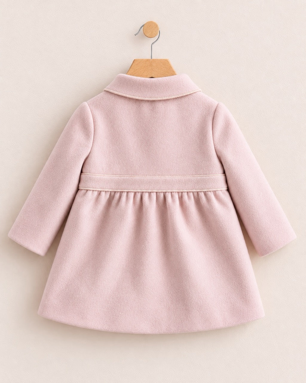 Backside of a light pink coat with a waist band, on a hanger against a muted pink background
