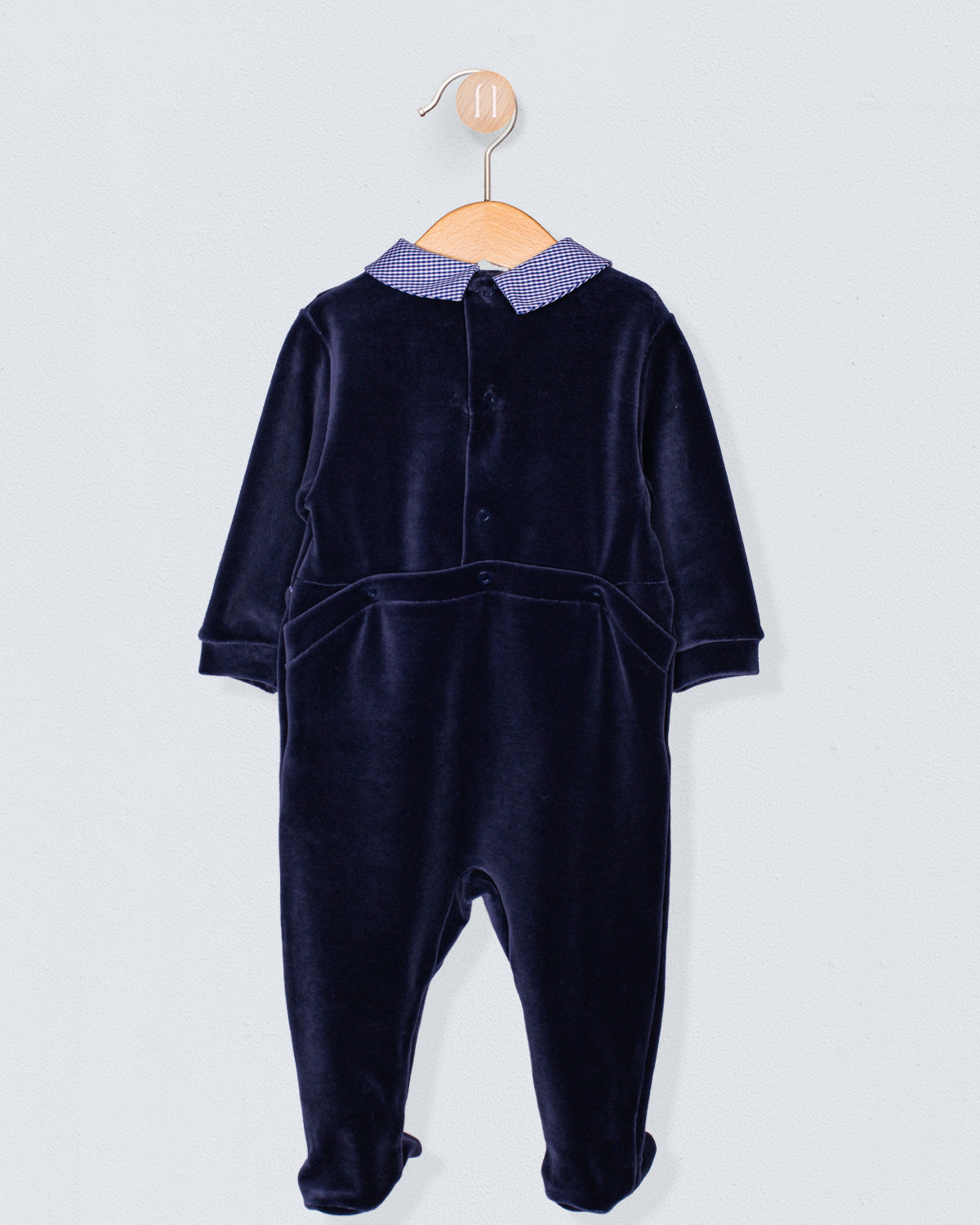 Back view of navy Italian velour footie featuring discreet snap closures along the panel seam and upper back, displayed on wooden hanger.