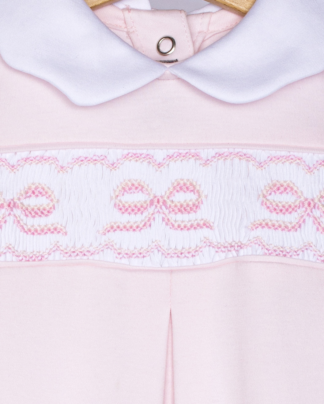 Close-up of a pink garment with white collar and embroidered details on a white background