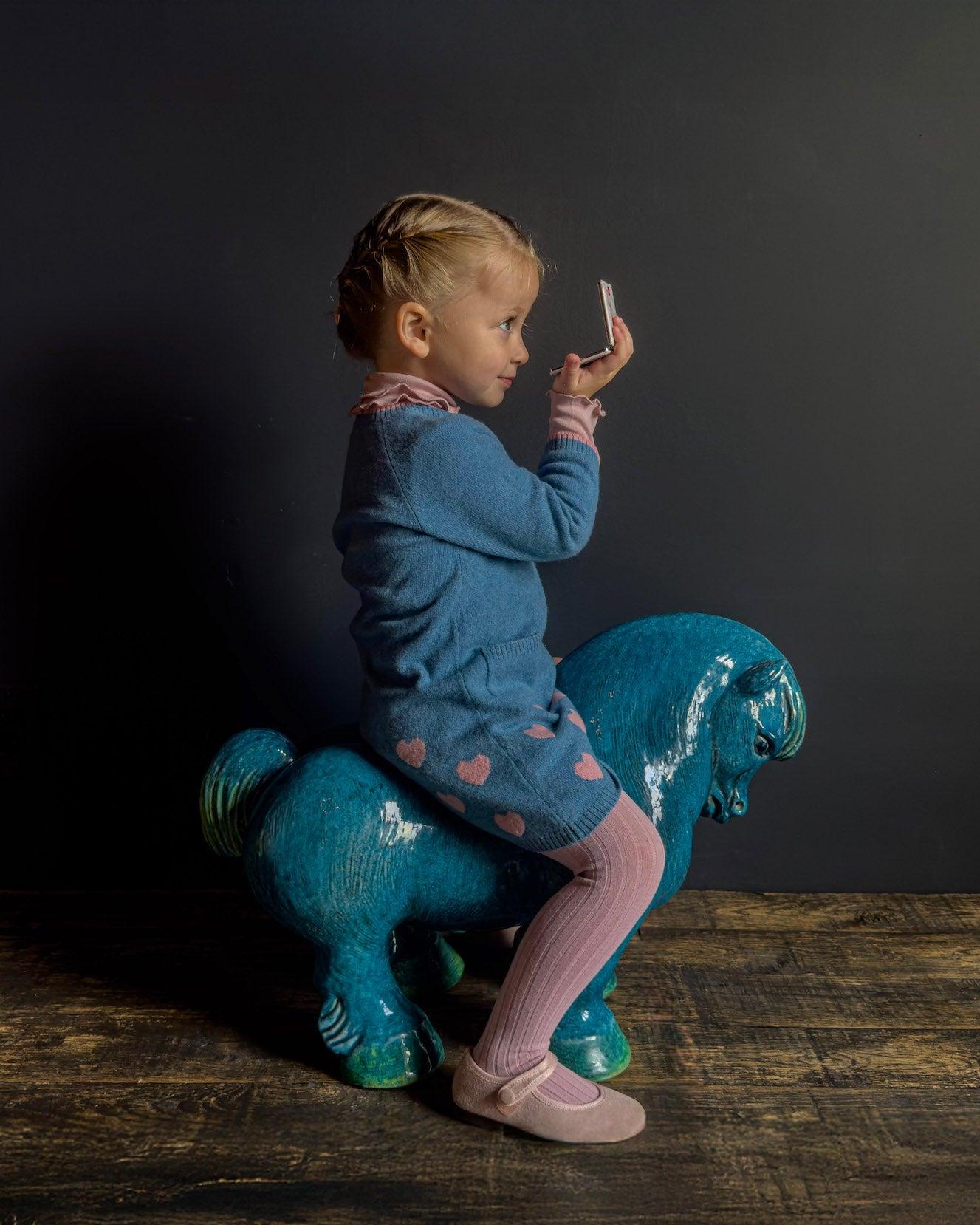 Child sitting on a blue horse toy against a dark background
