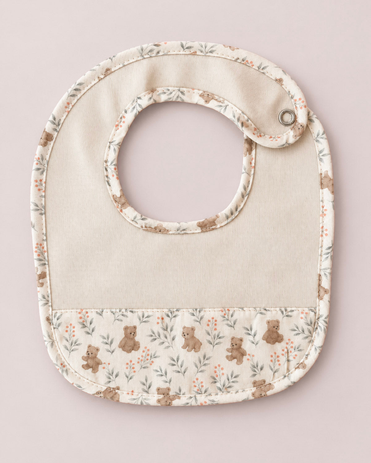 A baby bib with a cream-colored center and a floral and teddy bear patterned border, shown on a solid light pink background.