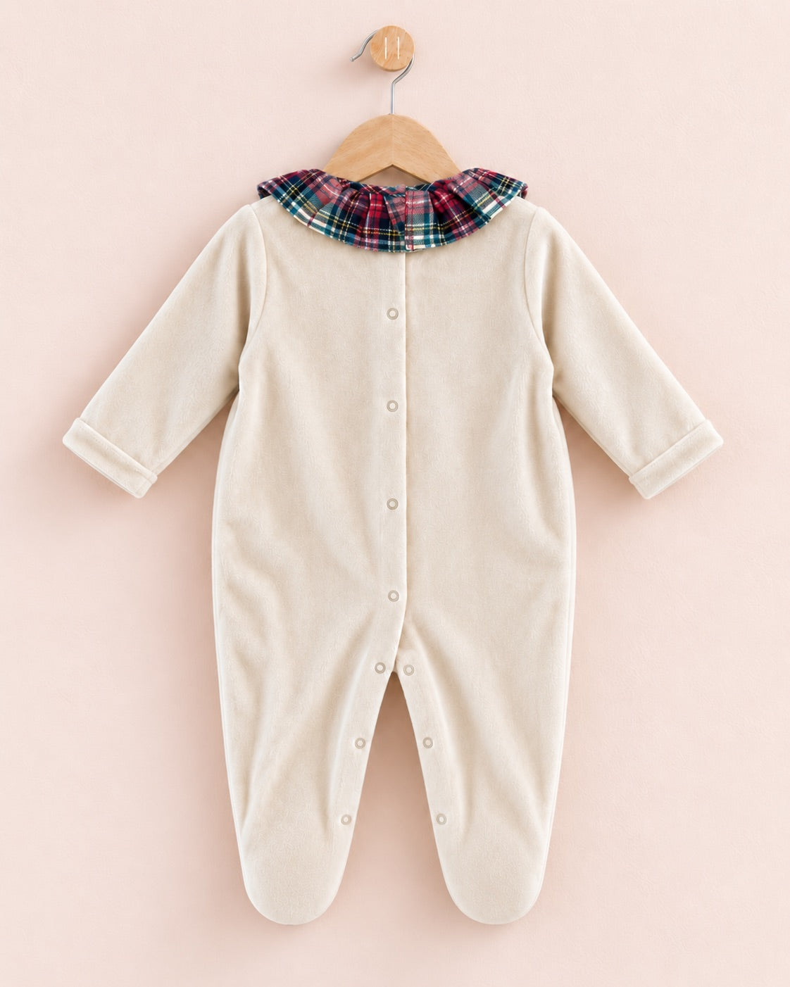 A cream-colored long-sleeve baby footed sleeper with a plaid collar, hanging on a wooden hanger against a soft pink background.