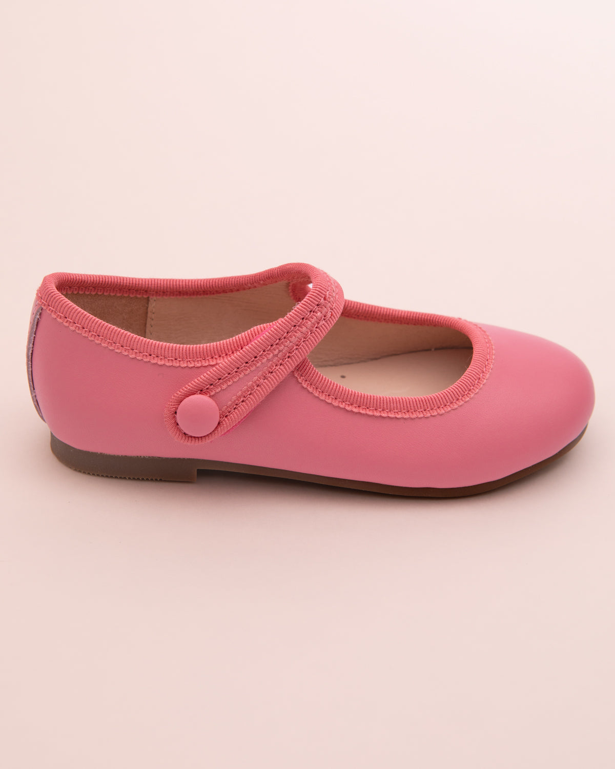 Side view of a single primrose leather Mary-Jane shoe with velcro strap, rubber sole, and tonal grosgrain trim on a light pink surface.