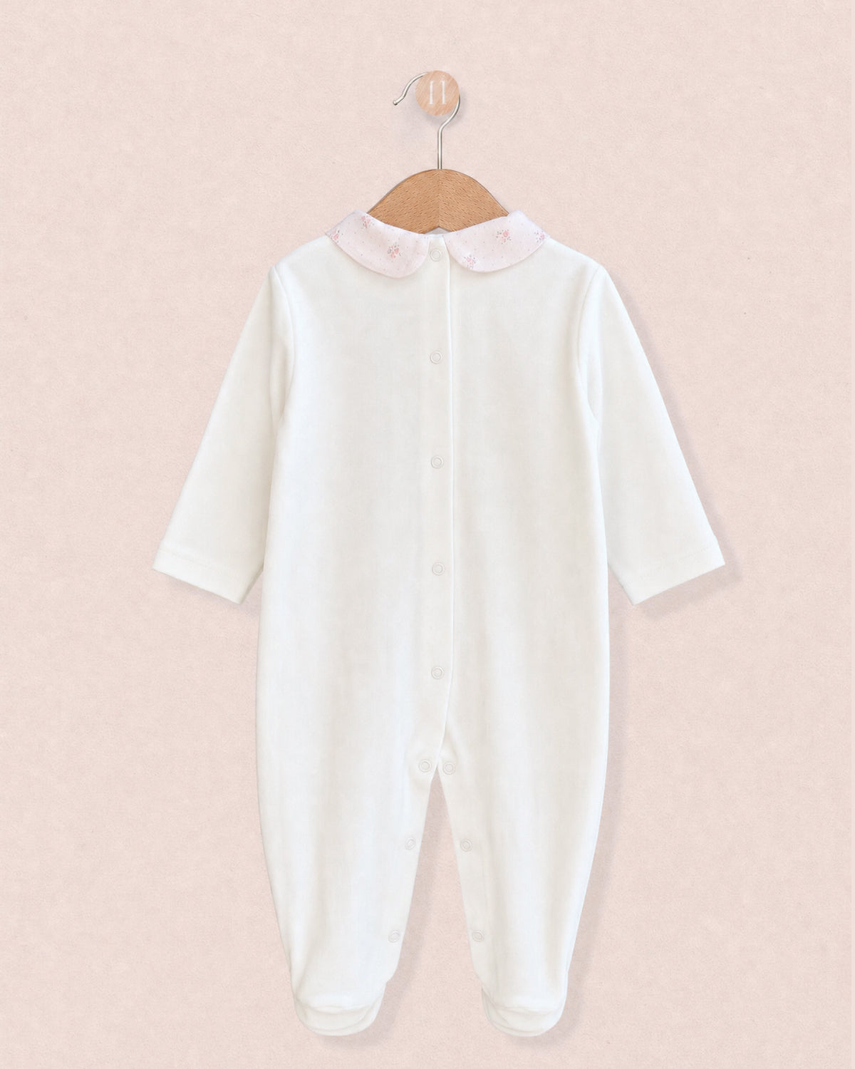 Back of white cotton baby onesie hanging from wooden hanger, with light pink floral motif collars.