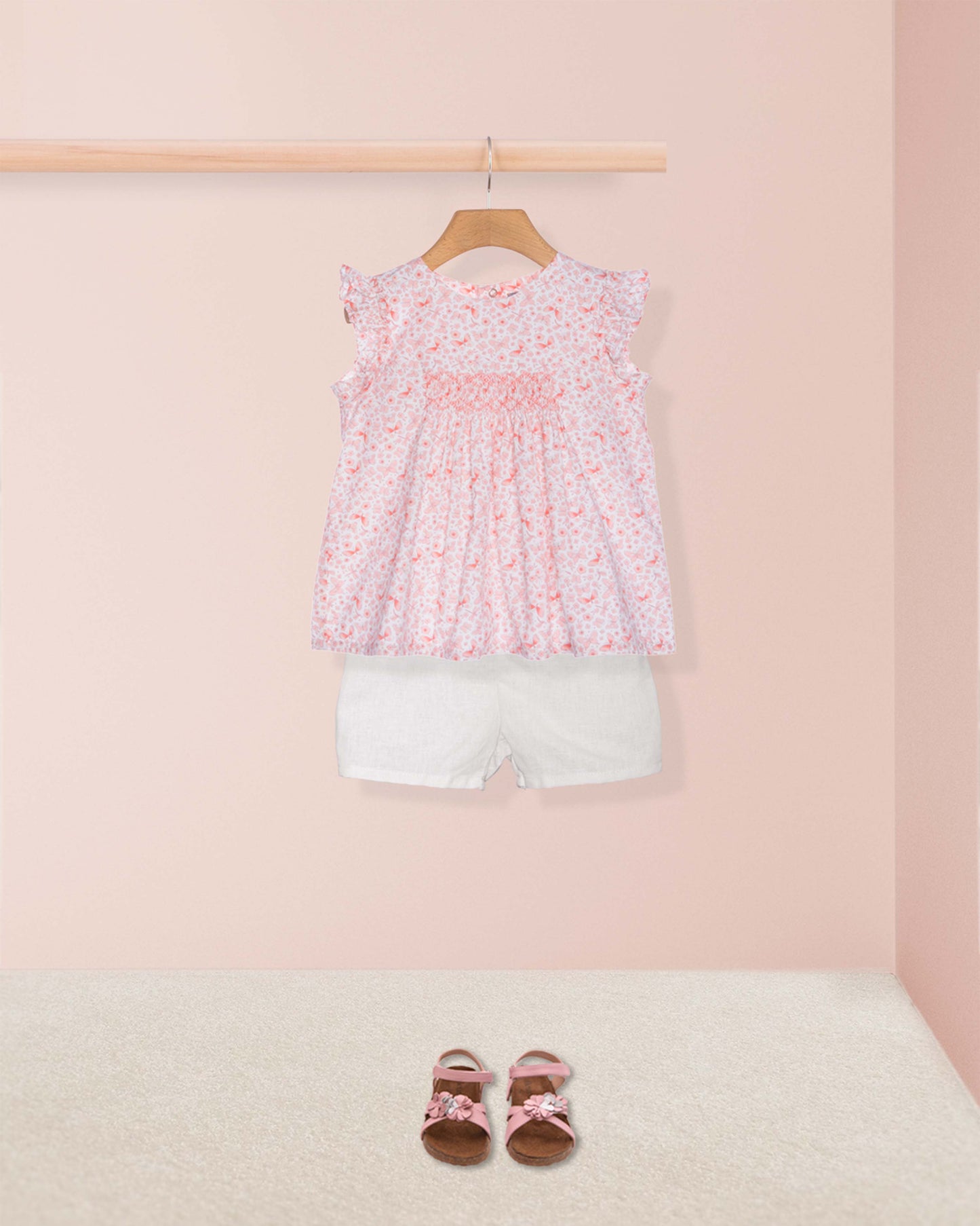 Children's outfit with floral top and white shorts on a pink background