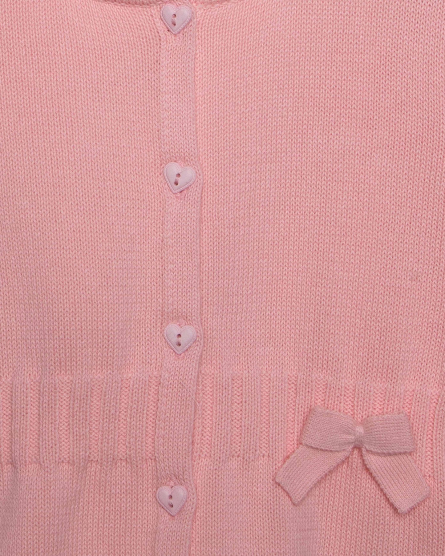 Close-up of a pink knitted cardigan with heart buttons and a bow detail.