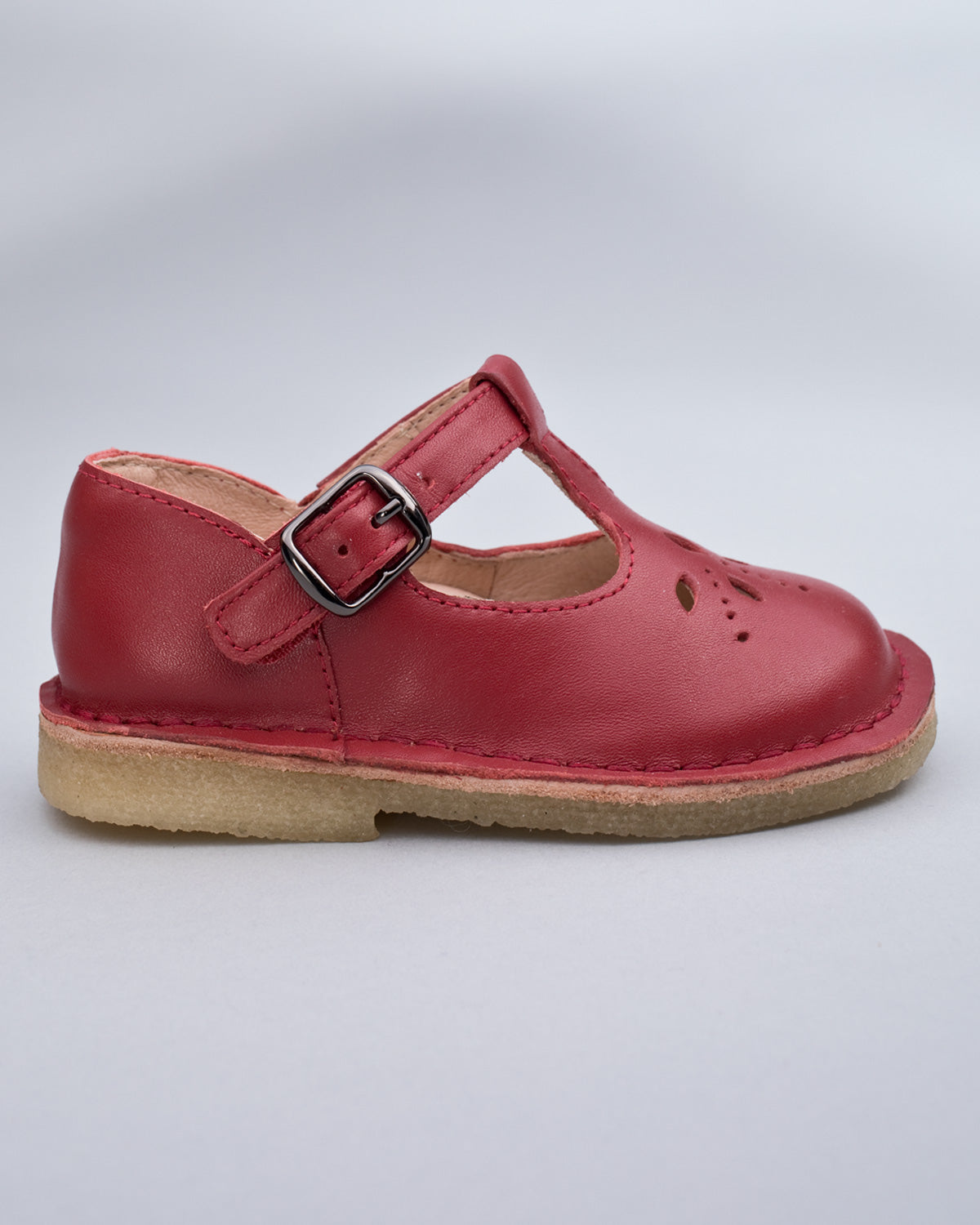 Side profile of a red leather crepe sole toddler shoe with velcro strap and buckle detail