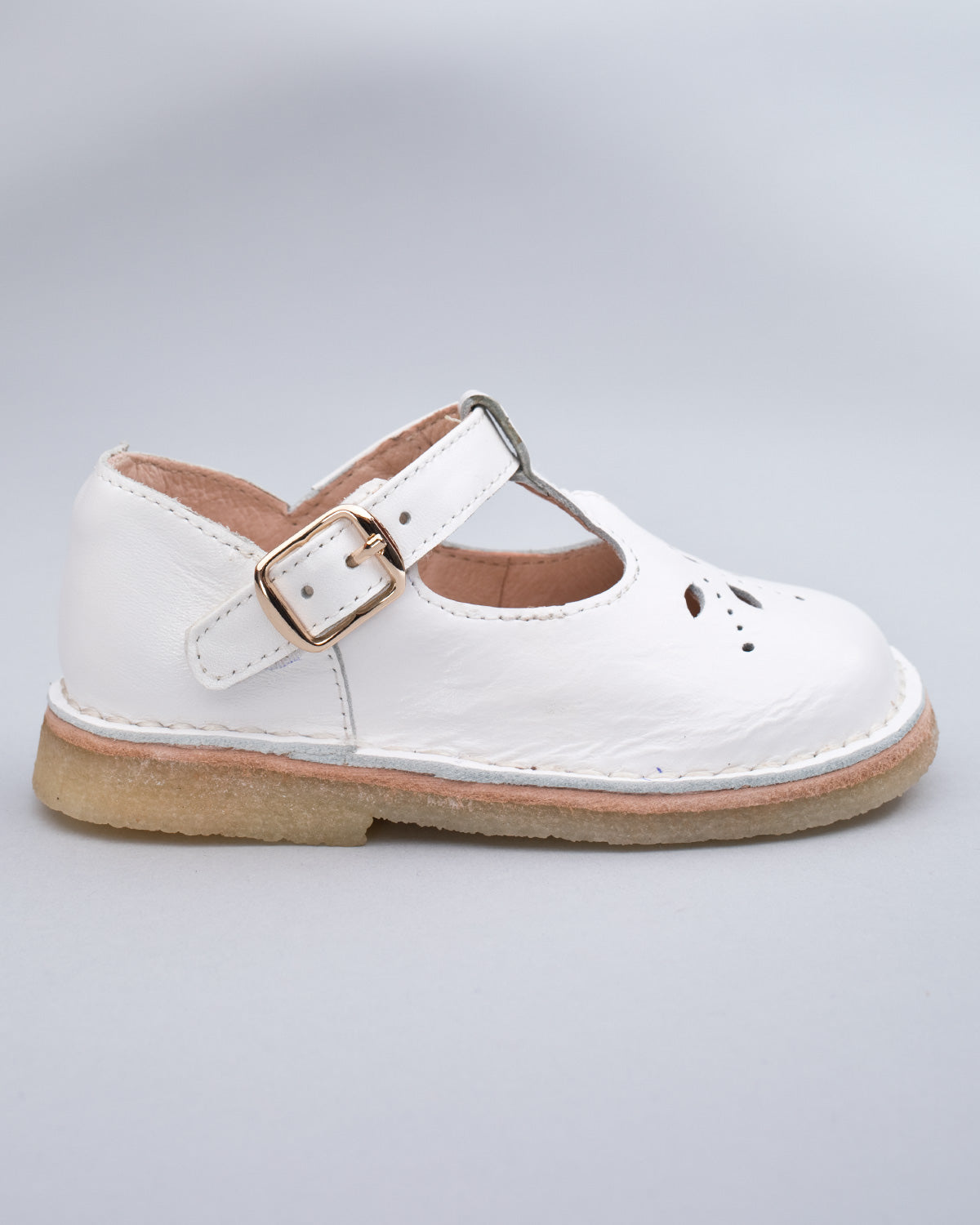 Side profile of a white leather crepe sole toddler shoe with velcro strap and buckle detail