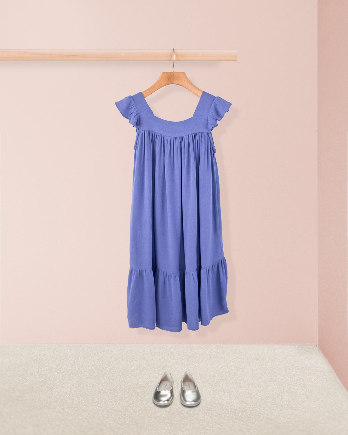 Slate ruffle dress styled with metallic toddler shoes hanging on a wooden hanger.