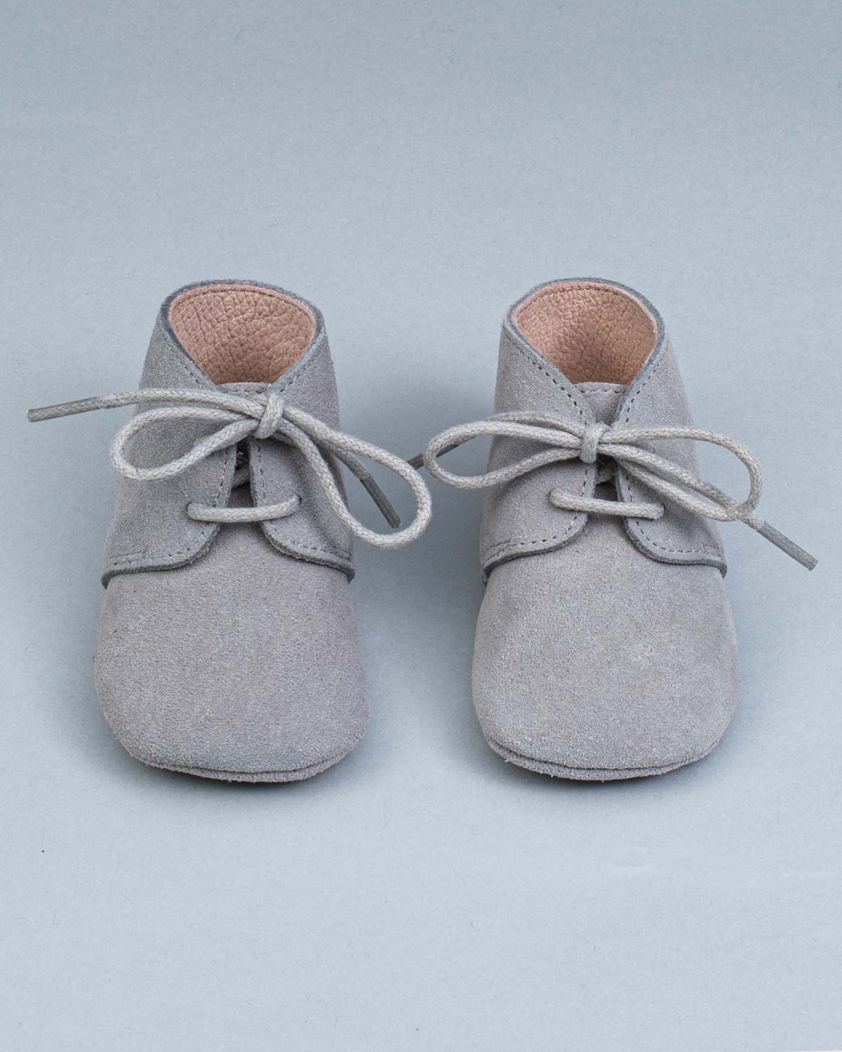 Front view of a pair of grey suede crib shoes with tied laces.