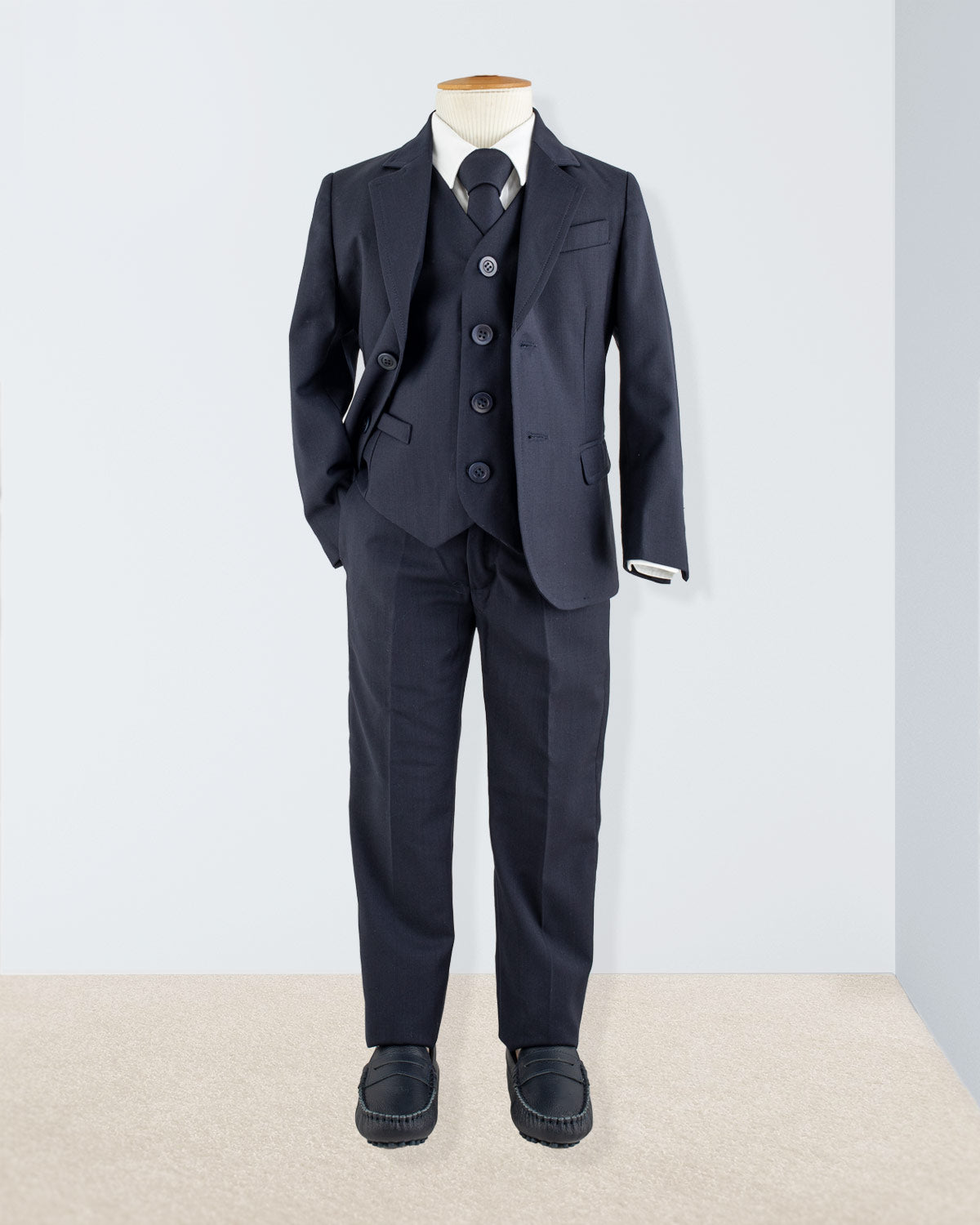 Complete boy’s formal outfit including navy jacket, vest, tie, shirt, and trousers on mannequin
