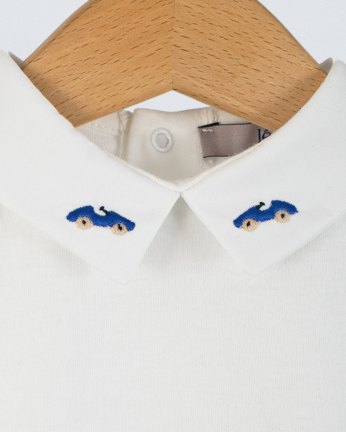 Close-up of the Andreas Baby Onesie’s collar, showing two royal blue cars with beige wheels embroideries on each side of the pointed collar.