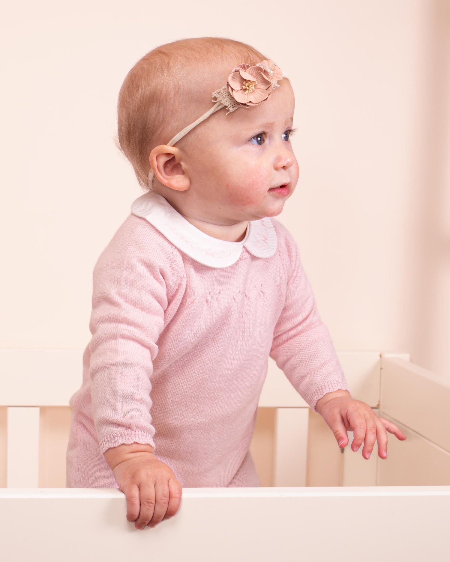 baby girl in crib looking sideways wearing pink romper