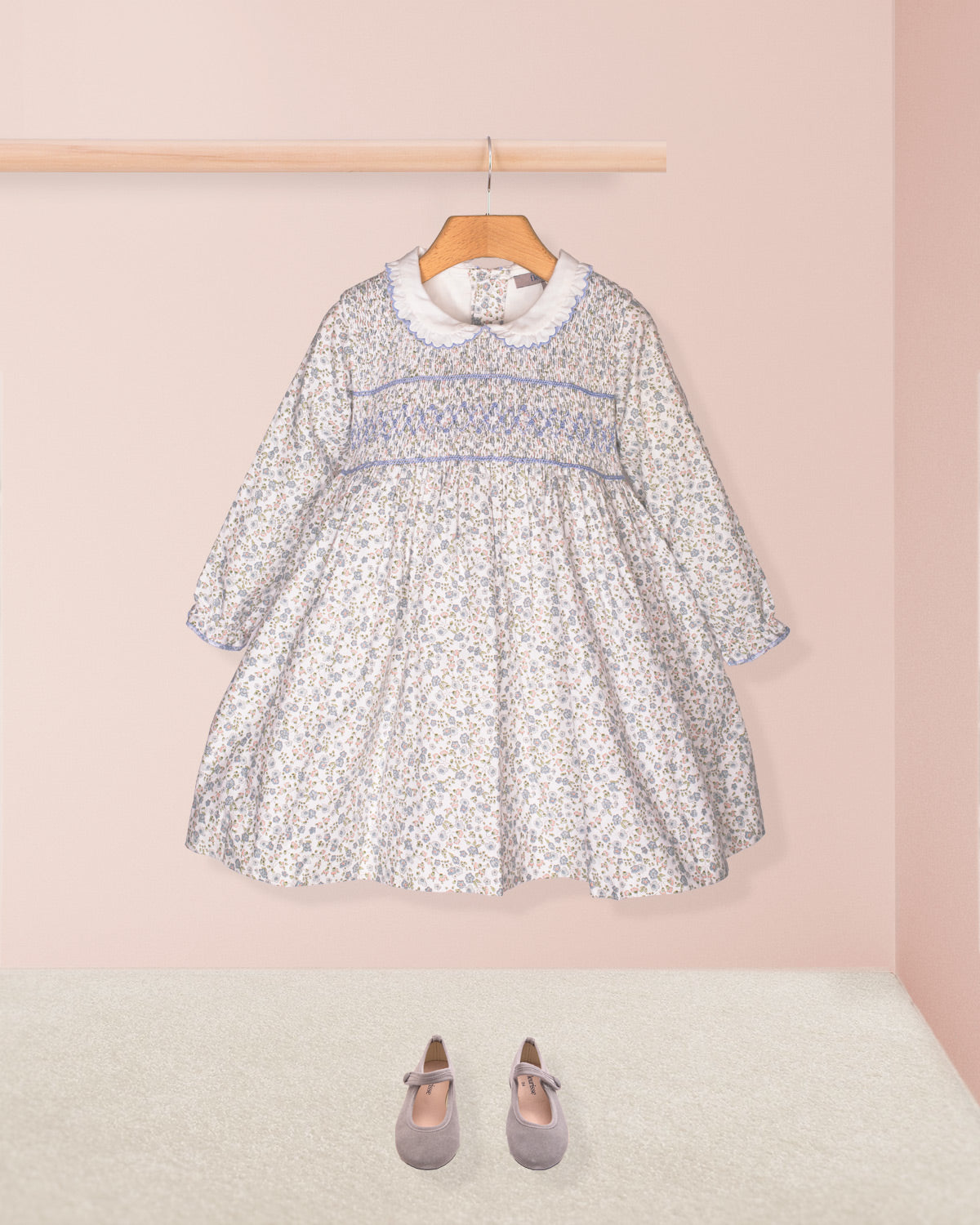 The Fiorella Belina dress styled with the Serena Cardigan in a soft blue knit and paired with navy blue Mary Jane shoes, displayed against a pastel pink backdrop.