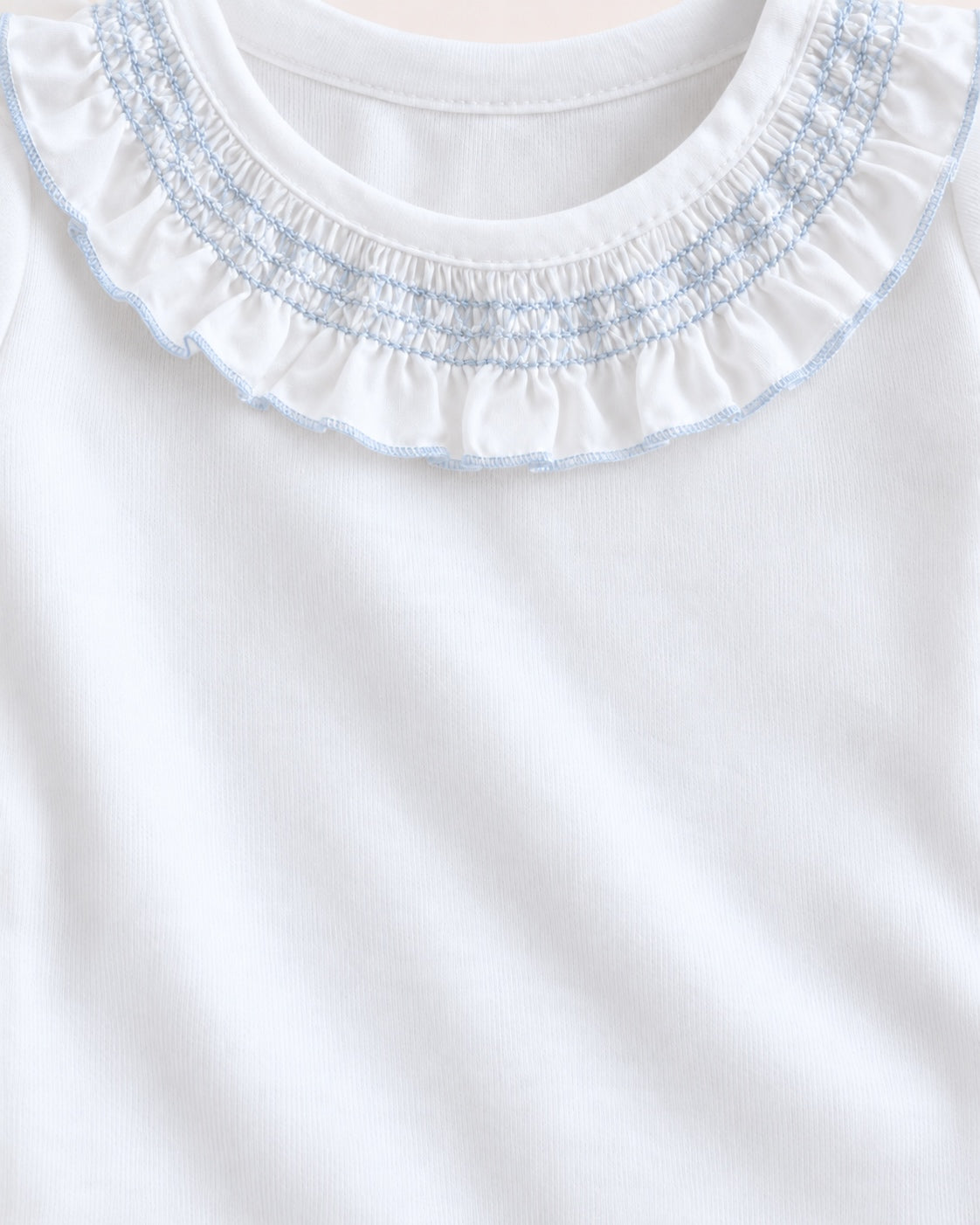 Close-up of a white baby or toddler top with a smocked ruffled collar in white and light blue.