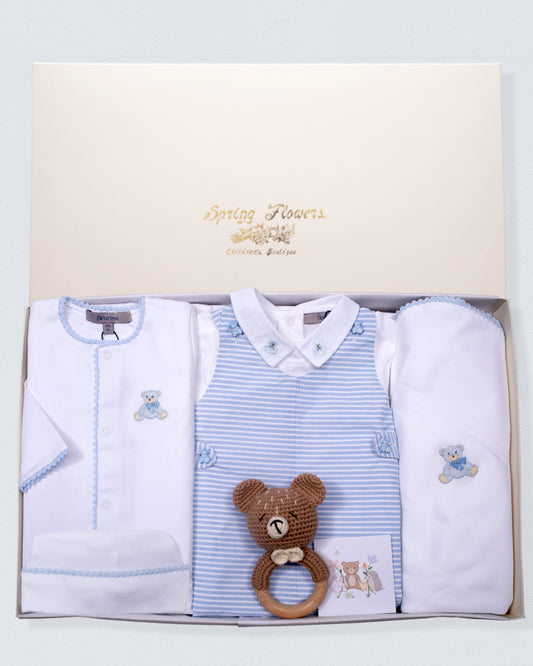 Baby clothing set with a bear rattle in a gift box on a light blue background