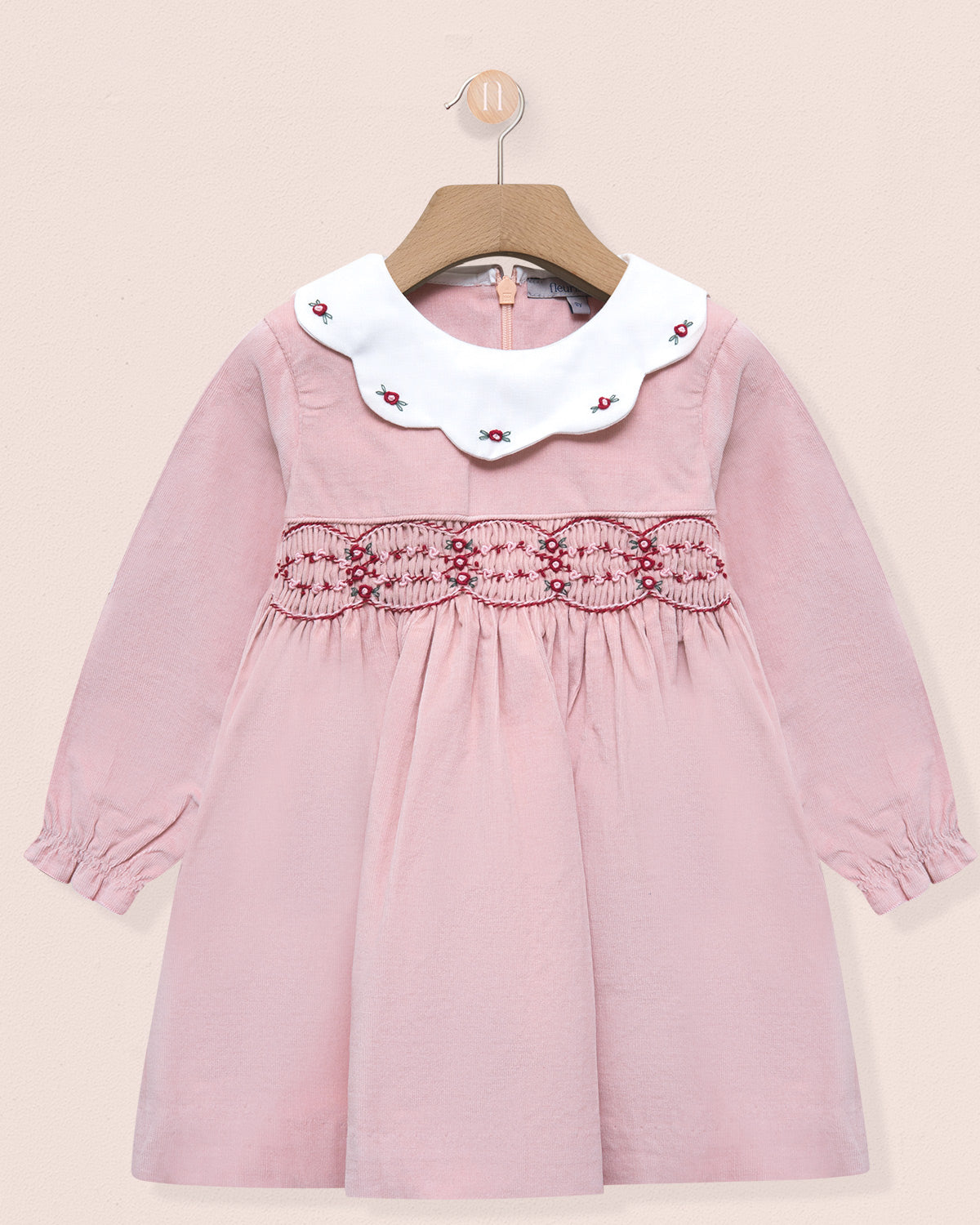 Pink dress with white collar and red embroidery on a beige background
