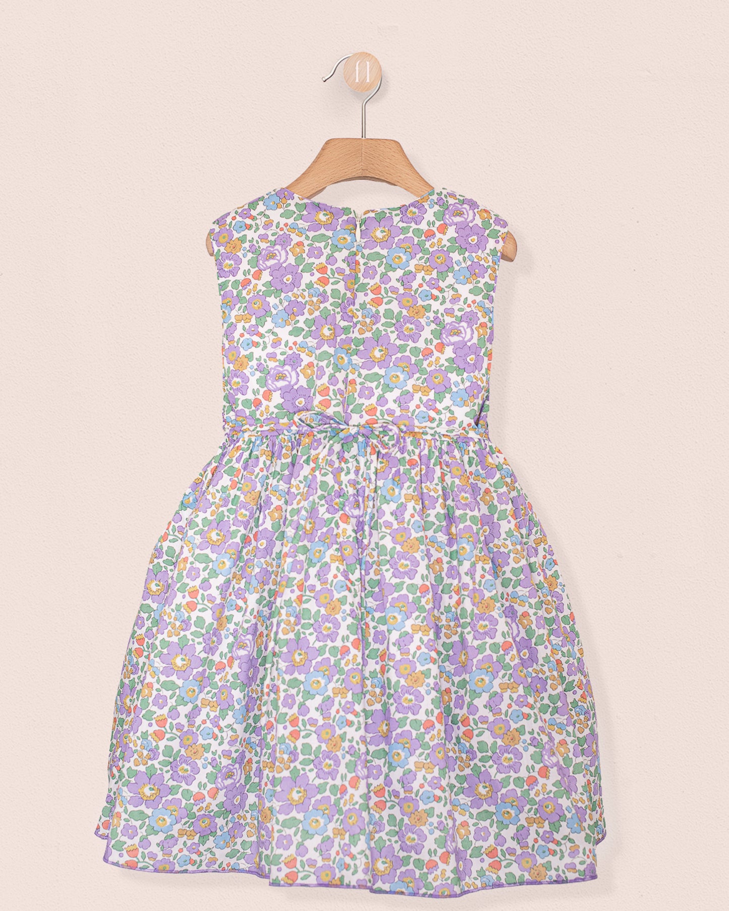 Back view of the Amandine Liberty Betsy Lavender Smock dress showing a zip closure and matching floral pattern, displayed on a wooden hanger
