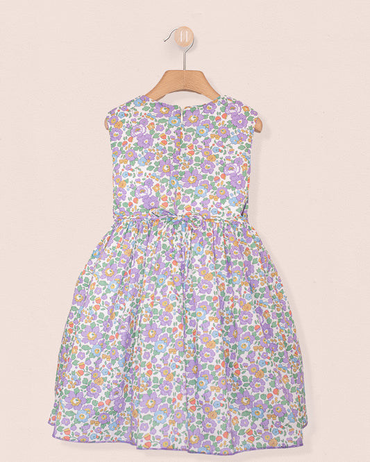 Back view of the Amandine Liberty Betsy Lavender Smock dress showing a zip closure and matching floral pattern, displayed on a wooden hanger